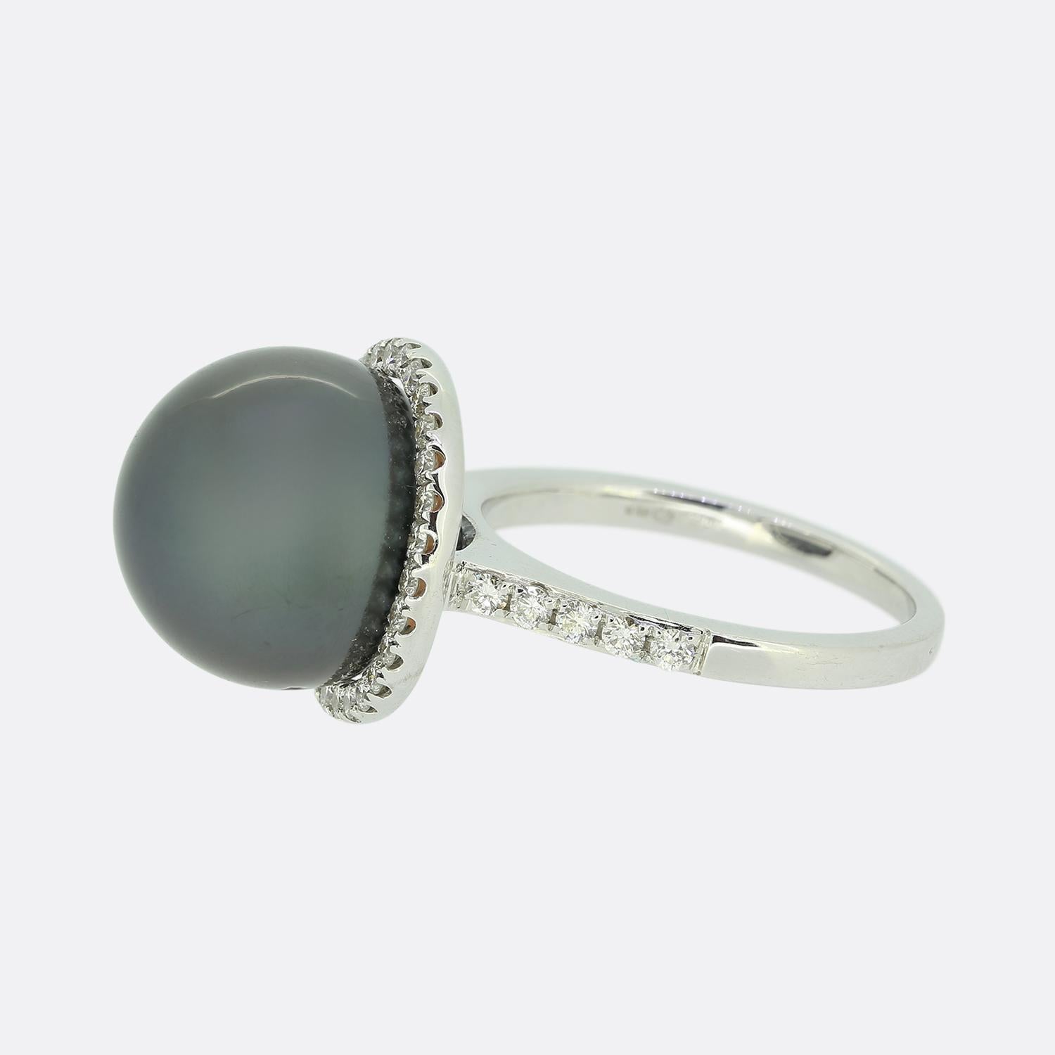 Hier haben wir einen auffälligen zeitgenössischen Clusterring. Dieses moderne Schmuckstück wurde aus 18 Karat Weißgold gefertigt und besticht durch eine schwarze Tahiti-Perle als Herzstück. Die stolze Perle ist von einem Halo aus runden weißen