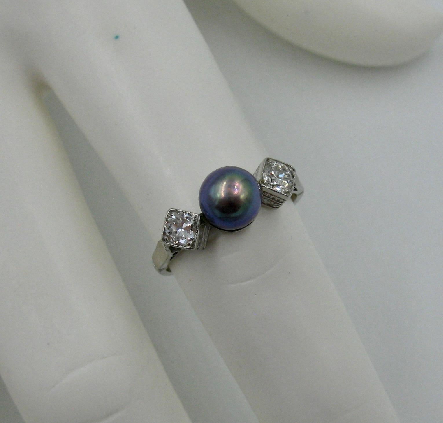 This is a stunning trilogy ring set with a central Black Pearl and two gorgeous sparkling round brilliant cut Diamonds in Platinum.  The dramatic combination of the black pearl and the white diamonds and platinum is gorgeous.  The pearl is 6 mm in