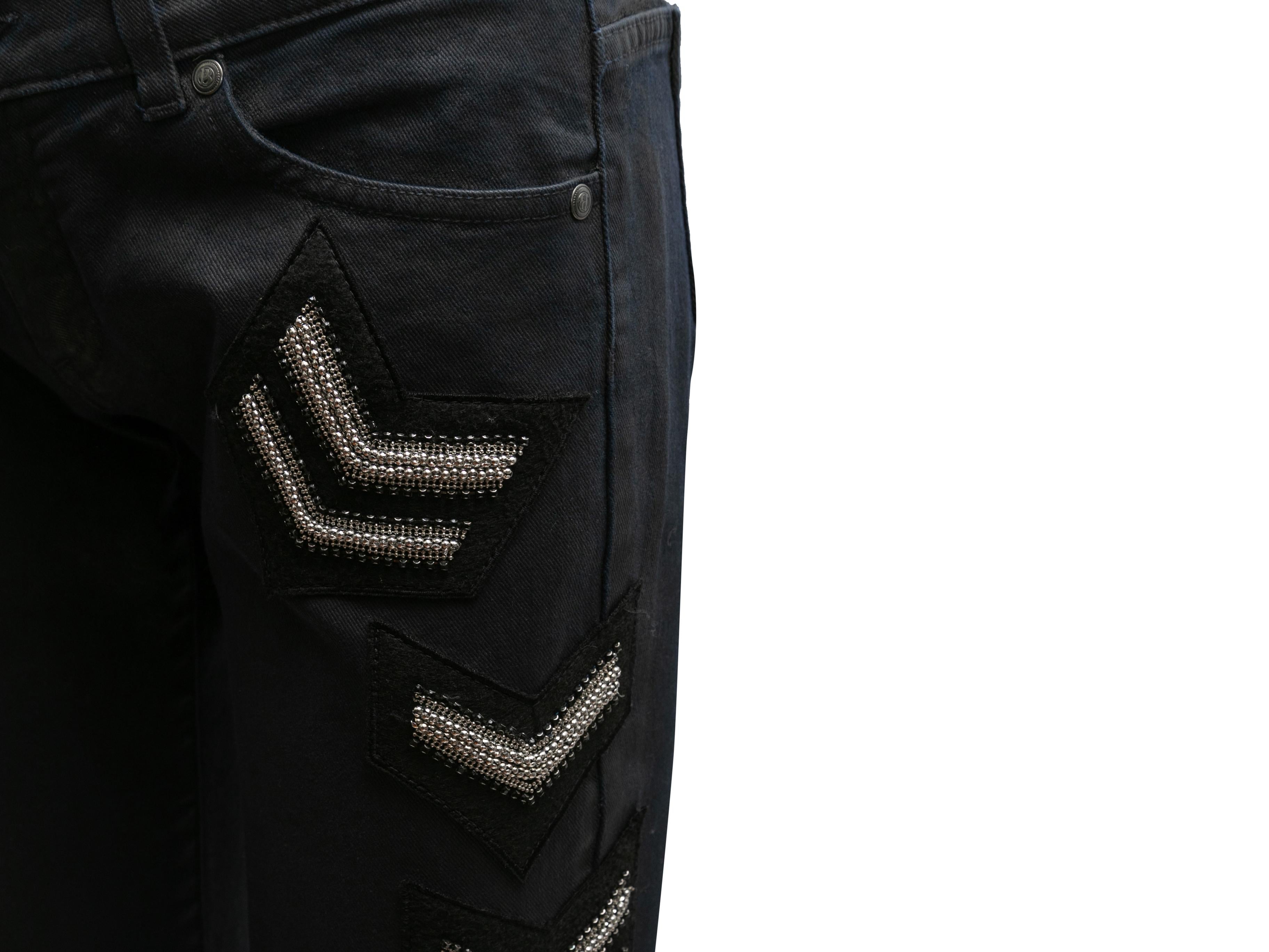 Black waxed denim skinny jeans by Pierre Balmain. Embroidered patch embellishments at side. Five pockets. Zip and button closures at front. 29