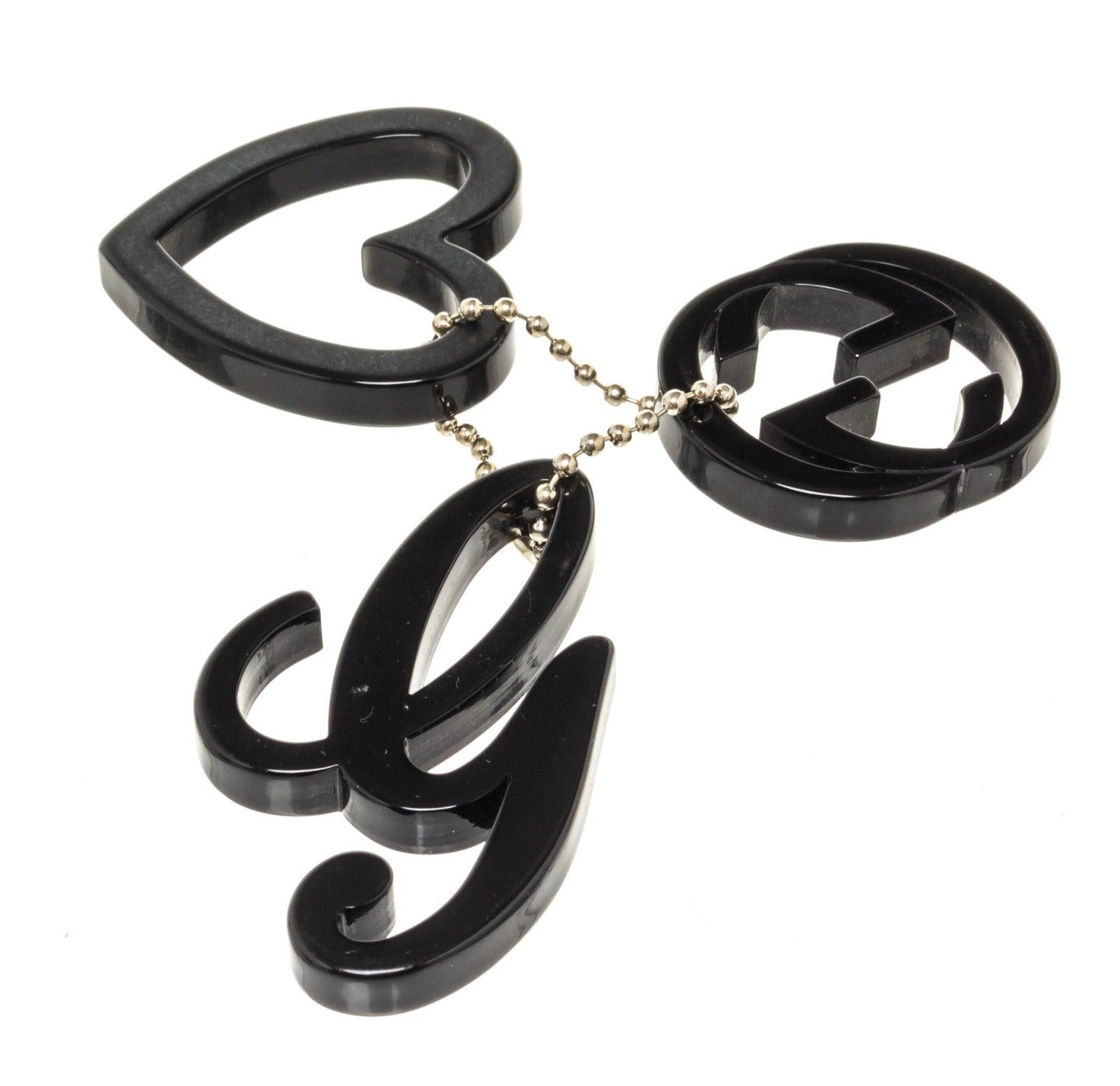 Black plastic Gucci bag charm features Gucci logo, heart symbol and G initial with silver-tone hardware.
 

47892MSC