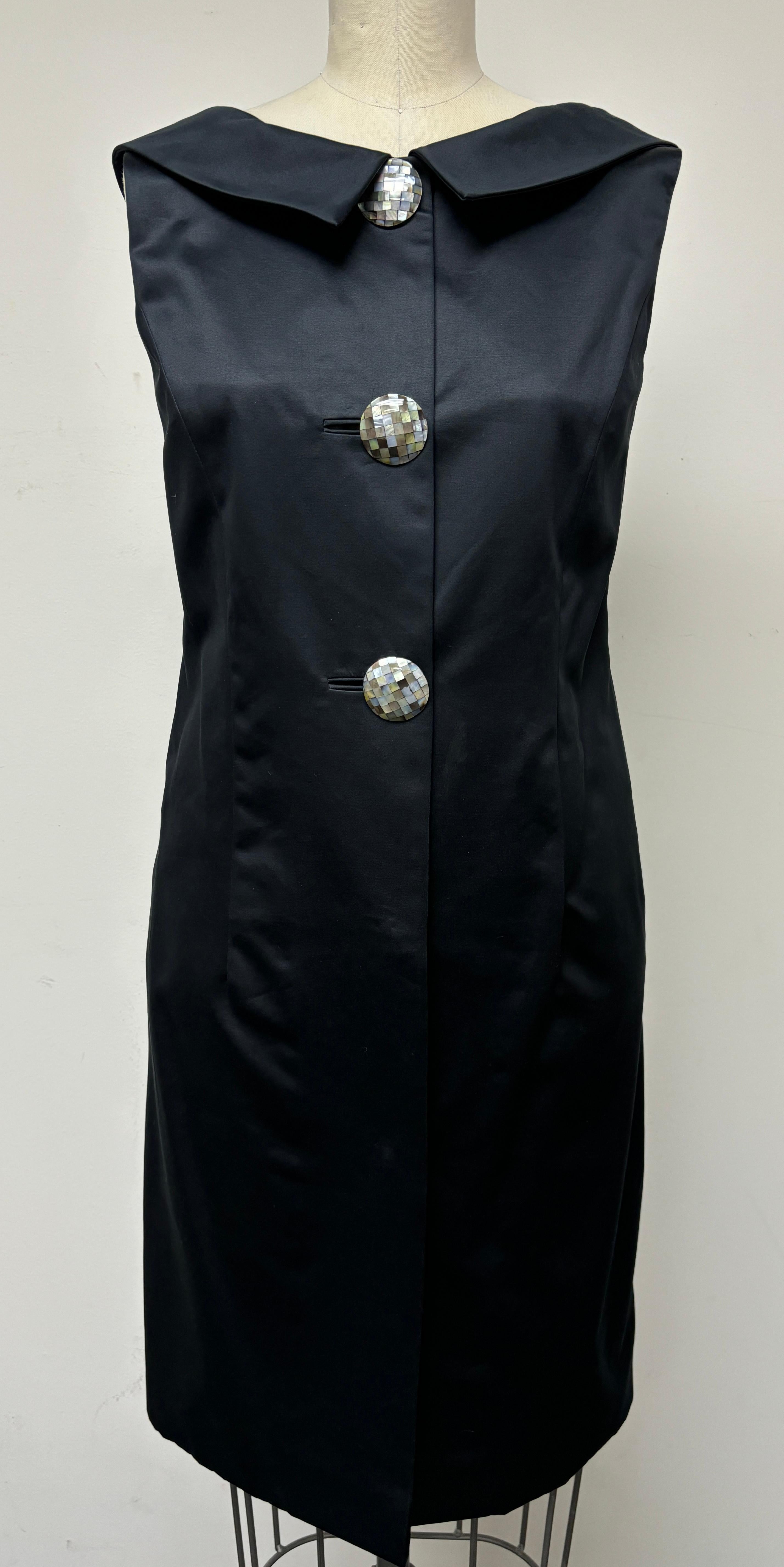 An elegant coat dress in black Swiss polished cotton with a wonderful silky look. Adorned with mother of pearl mosaic buttons. The 60's style and gathered back collar is perfect for day  into evening with its eye-catching design. The back of the