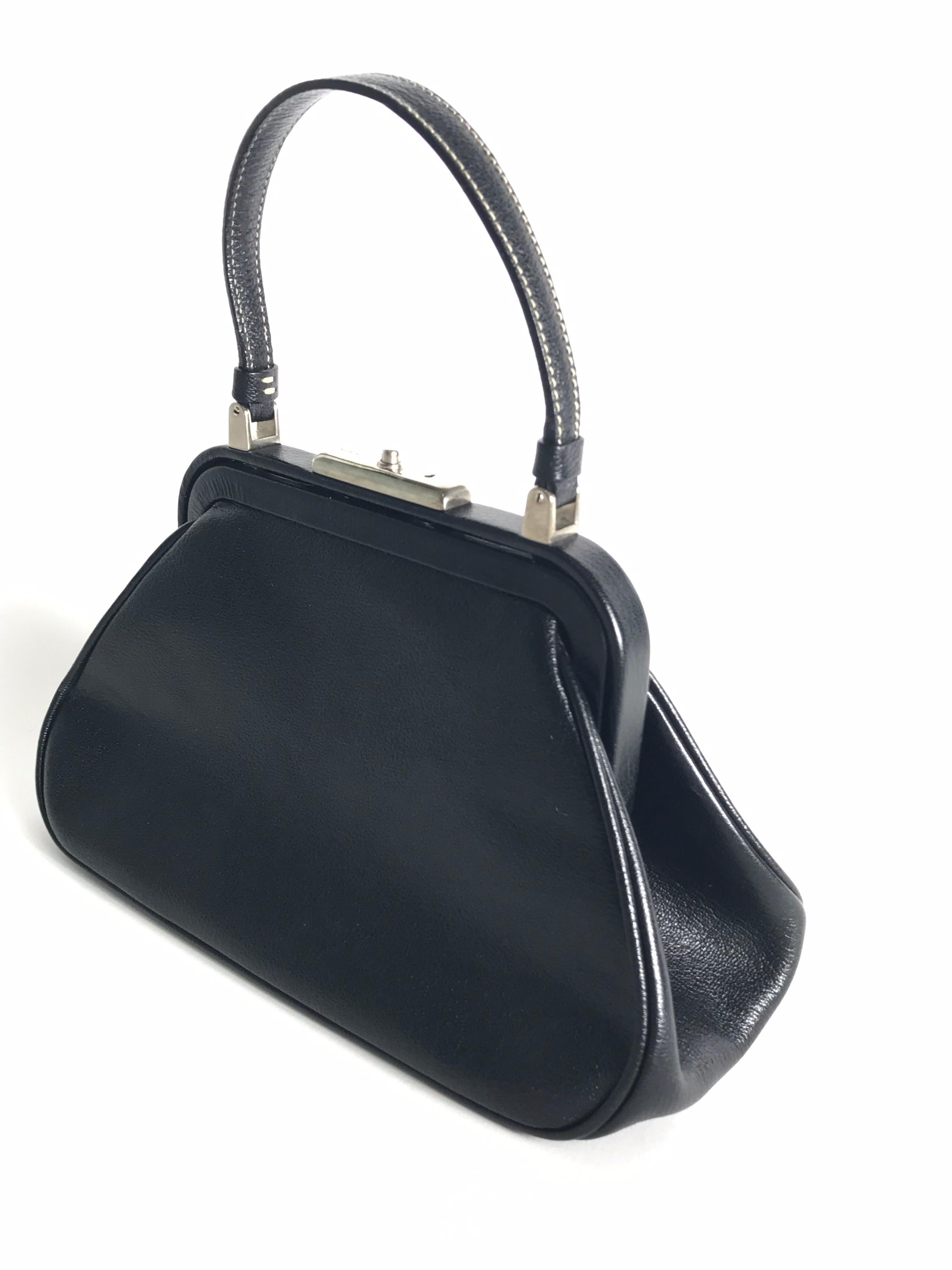 Black leather Prada mini frame bag with silver-tone hardware, creme contrast stitching throughout, single flat top handle, tonal logo jacquard lining, single zip pocket at interior wall and push-lock closure at top. Includes keys. Condition: