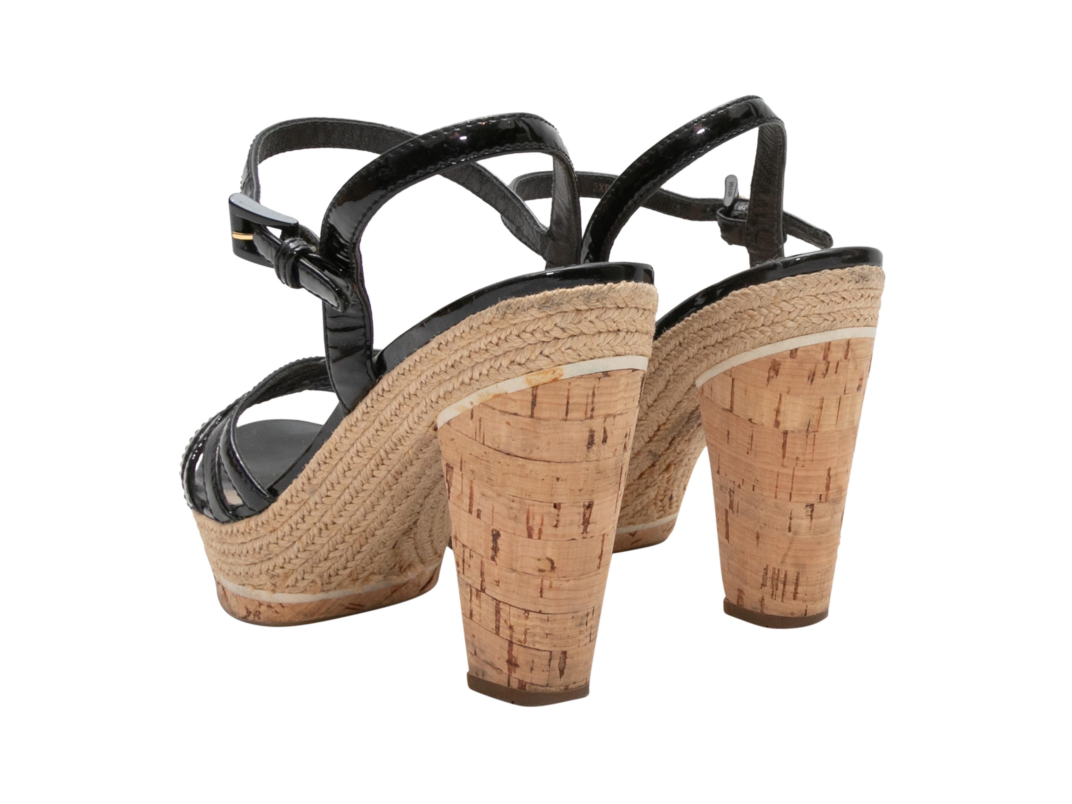 Black patent leather strappy espadrille heeled sandals by Prada. Jute trim at cork heels. Buckle closures at ankle straps. 1