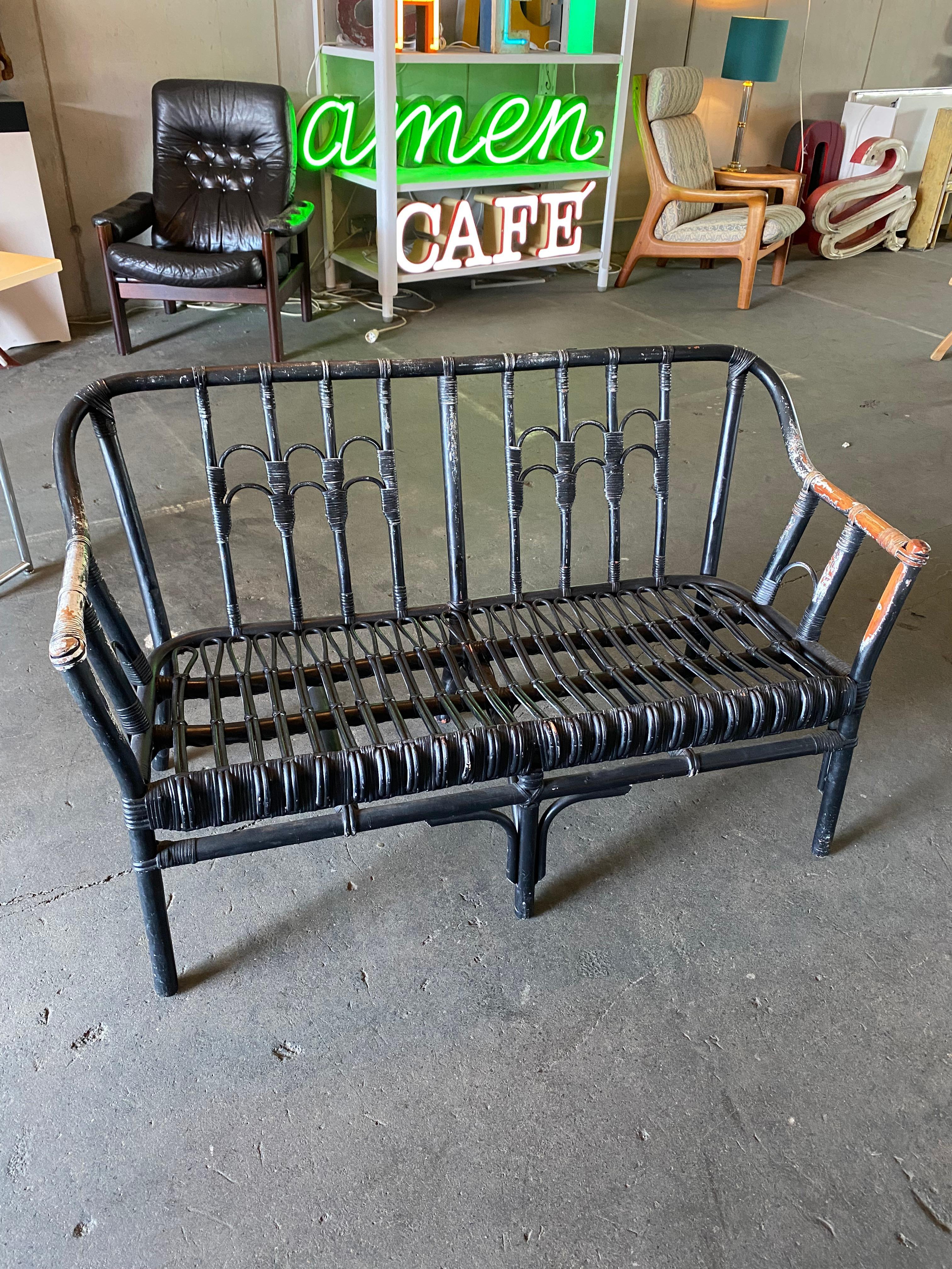 Schwarze Bank von Decartiv. Es ist aus Rattan, ursprünglich weiß, hat aber lackiert und zweite Schicht schwarz. Dieser Vintage-Look passt perfekt zum trendigen Boho-Einrichtungsstil. Die Bank erinnert an den Peacock Chair, der ebenfalls aus Rattan