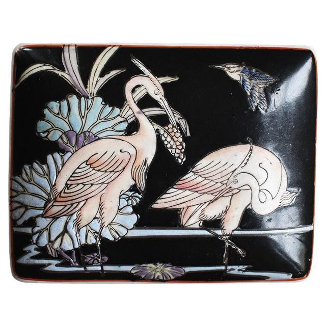 A pretty chinoiserie ceramic decorative trinket box with a lid. Painted in black. the sides and top are decorated with pink cranes in water, surrounded by blue and purple lotus flowers. This would be a fabulous gift, or for use on a side table or