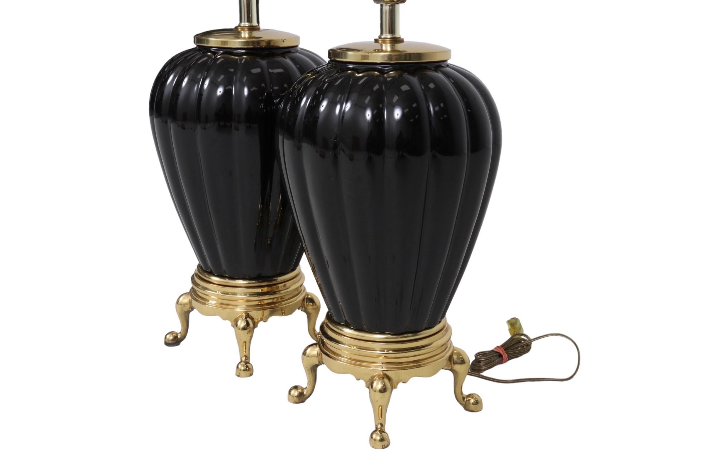 A pair of black ceramic table lamps. Ribbed baluster vases rest on brass bases raised on cabriole legs and finished with pad feet. Wired and working. Each lamp measures 9.5