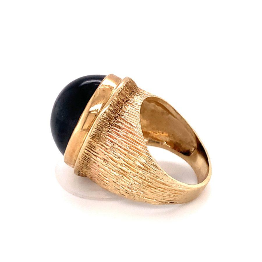 One black sapphire 14K yellow gold cocktail ring featuring one bezel set, oval cabochon black sapphire weighing approximately 30 ct. The mount features a hand-textured, lined finish throughout.

Sleek, funky, edgy.

Additionbal information:
Metal: