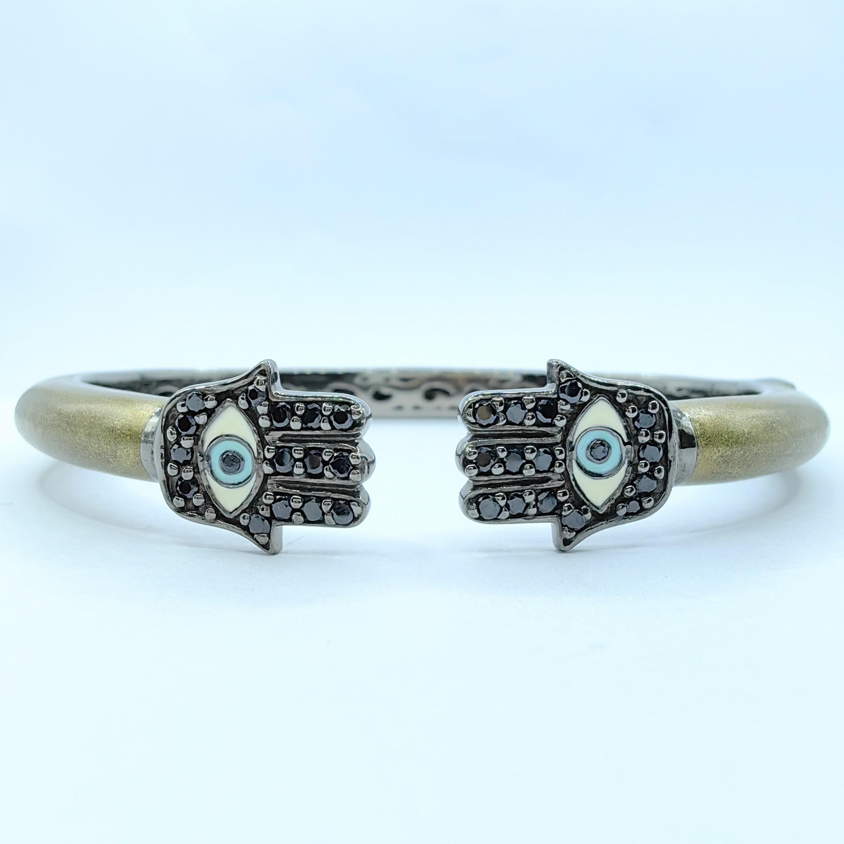 This striking Black Sapphire and Shimmery Enamel Hamsa Evil Eye Cuff Bracelet in Sterling Silver exudes both elegance and mysticism, with its symbolic design and luxurious materials. Crafted in sterling silver, it features 0.59ct of round-cut black