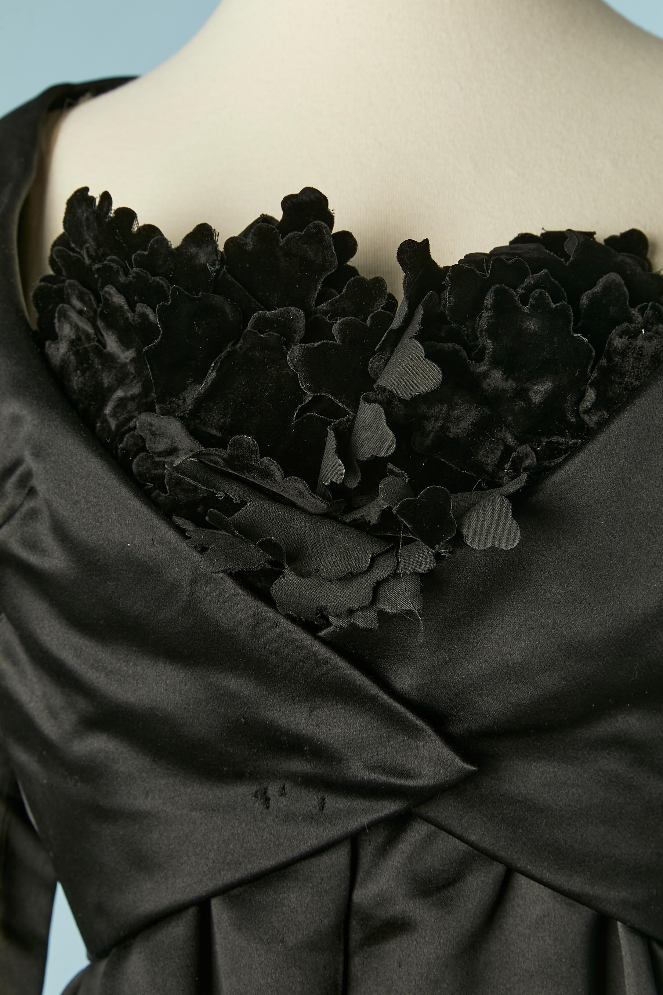 Schwarzes Boléro- und Bustierkleid aus Satin mit schwarzen Samtblumen auf der Büste. Futter aus Seidenorganza. Druckknopfverschluss an der Jacke und auch am Kleid in der vorderen Mitte. Der Boléro ist auf dem Kleid aufgenäht und es ist mit Knochen