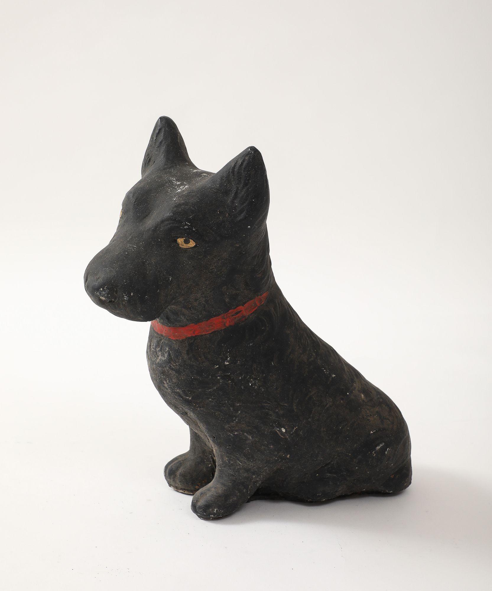 Unique reconstituted stone garden statue in the shape of a black painted Scottie dog with red paint collar, and amber eyes. Made in England in the Mid 20th century, this charming statue is a playful element to add to the landscape. Good condition,