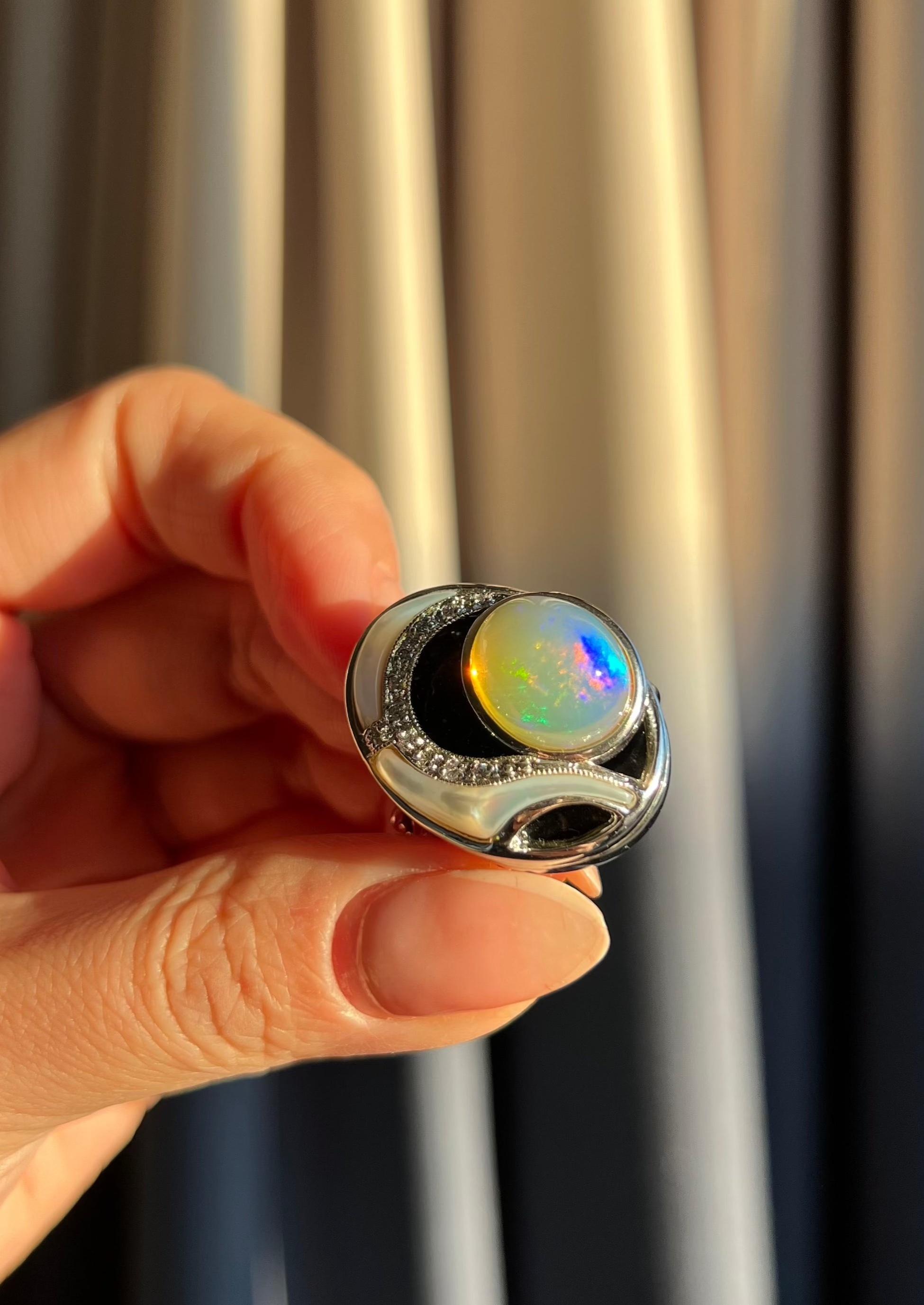 This stunning statement ring showcases a cabochon opal set beneath onyx, accented with Mother of Pearl carvings, pavé clear sapphires, and two chrome diopsides on the band. Its exquisite craftsmanship exudes timeless sophistication and