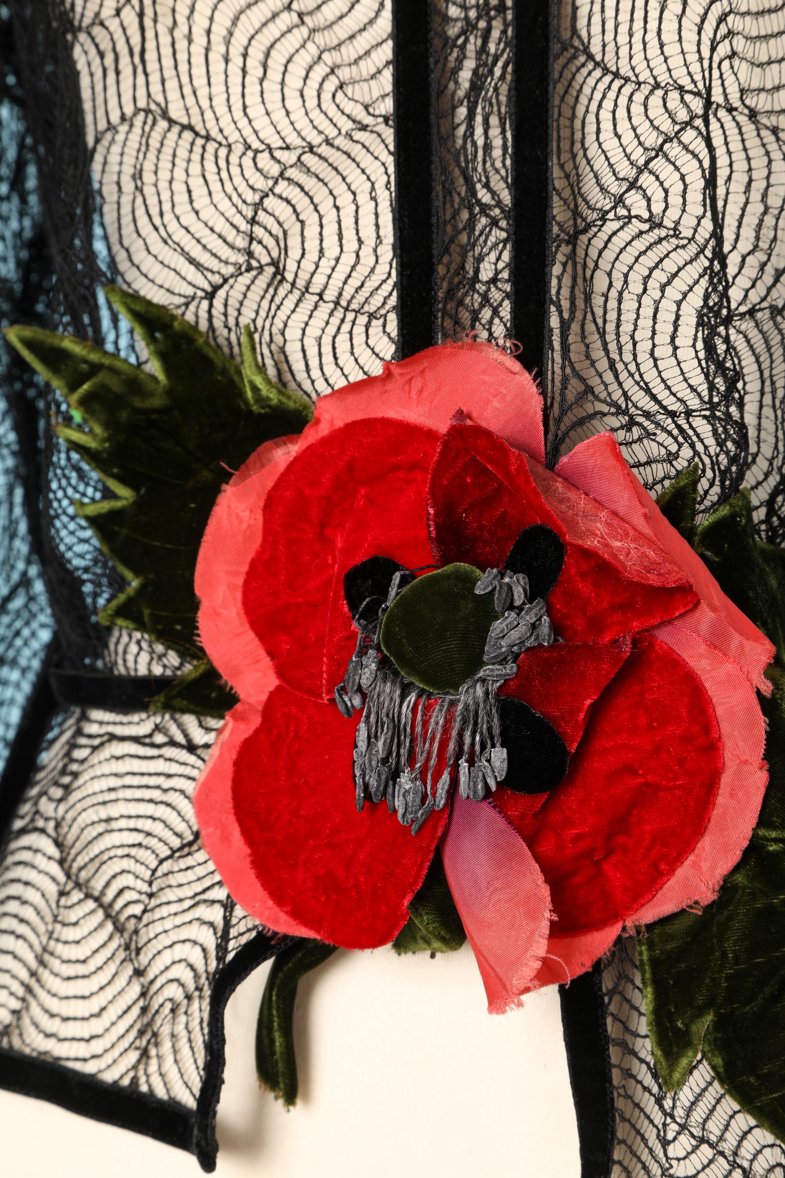Chemisier noir en dentelle transparente avec fleur en velours. Passepoil en ruban de velours noir. Ruban noir à nouer derrière le cou et crochet au milieu du dos sur la taille. 
TAILLE M 