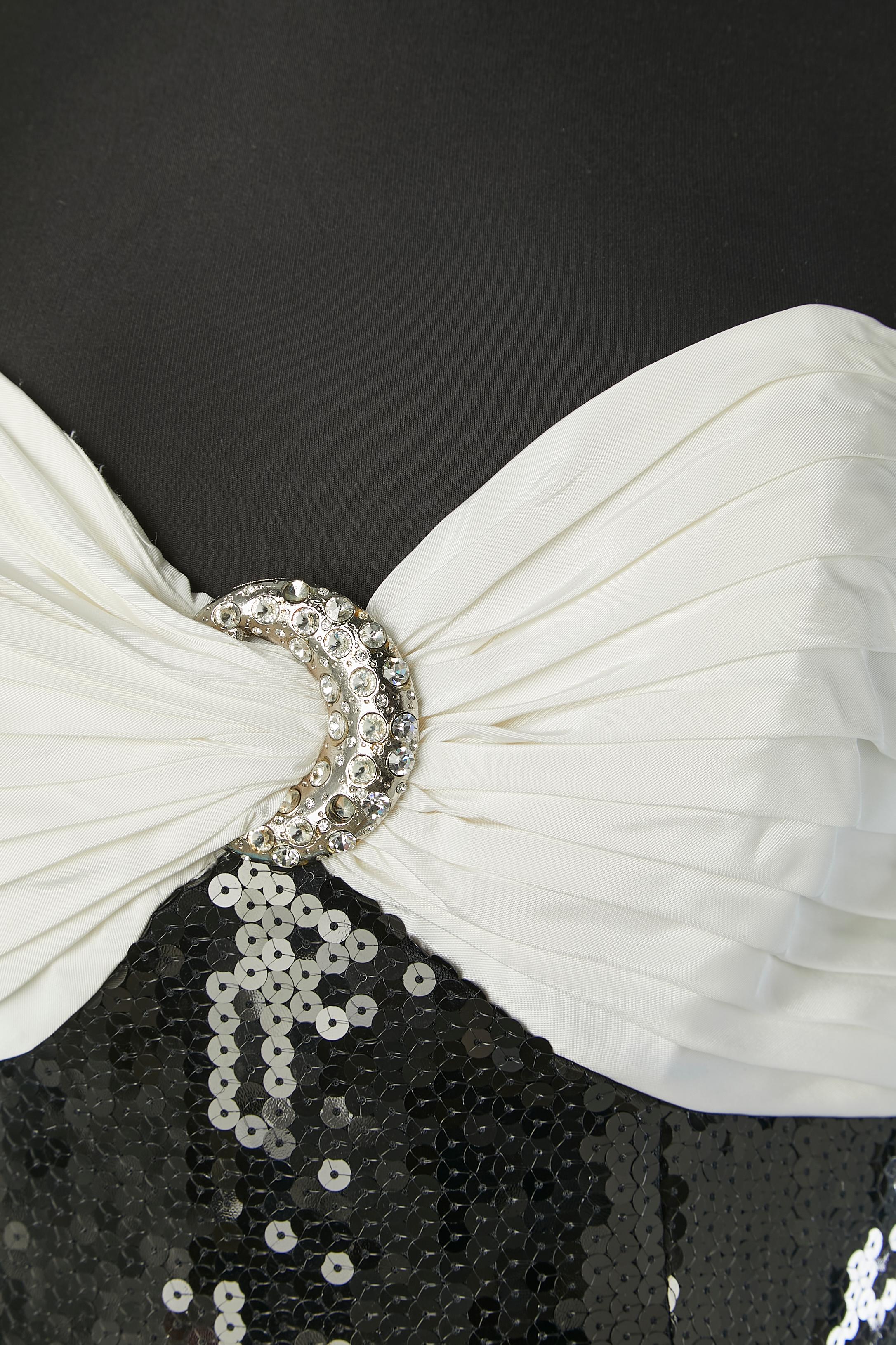 Abito da sera bustier in paillettes nere con volant bianchi. Composizione del tessuto principale: 100% poliestere. A contrasto (volant bianchi): 100% acetato. Composizione della fodera: 100% poliestere. Bustier disossato. Chiusura con zip e gancio