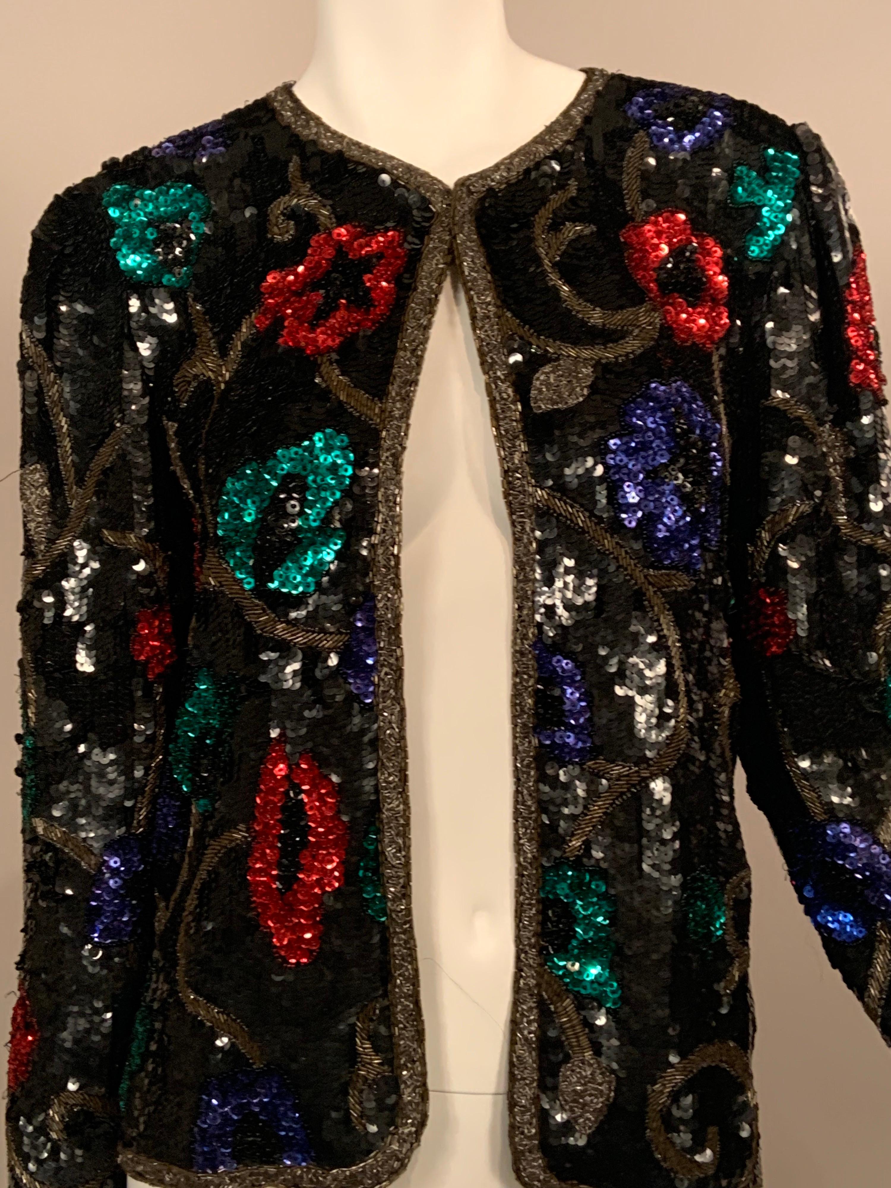 This vintage cardigan style jackt has a black sequin background and it is edged with silver and gold bugle beads.  The body of the jacket has red, blue and green sequin flowers with caviar beaded centers and edging.  These are on a meandering leaf
