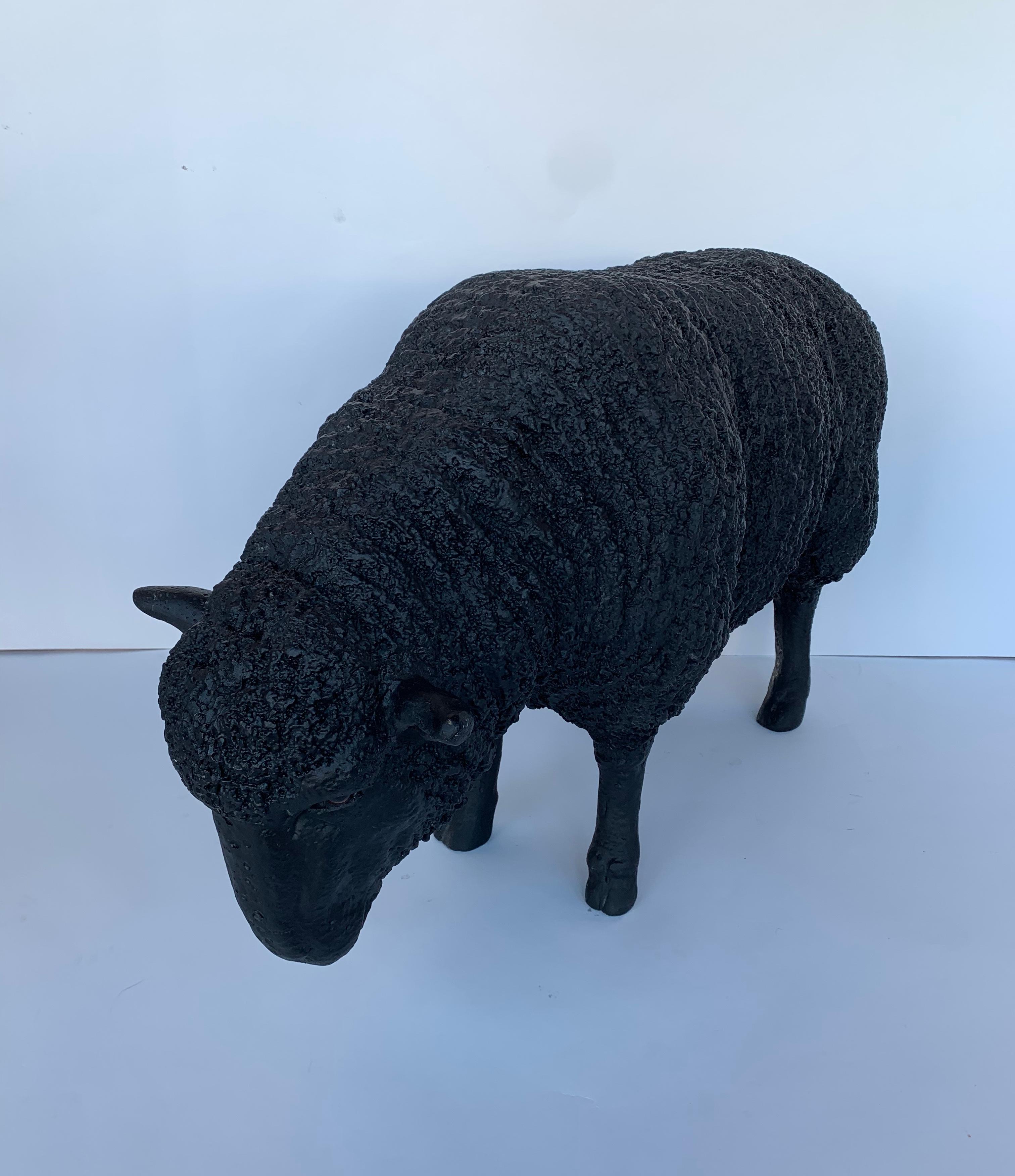 Black fiberglass sculpture of a sheep grazing.