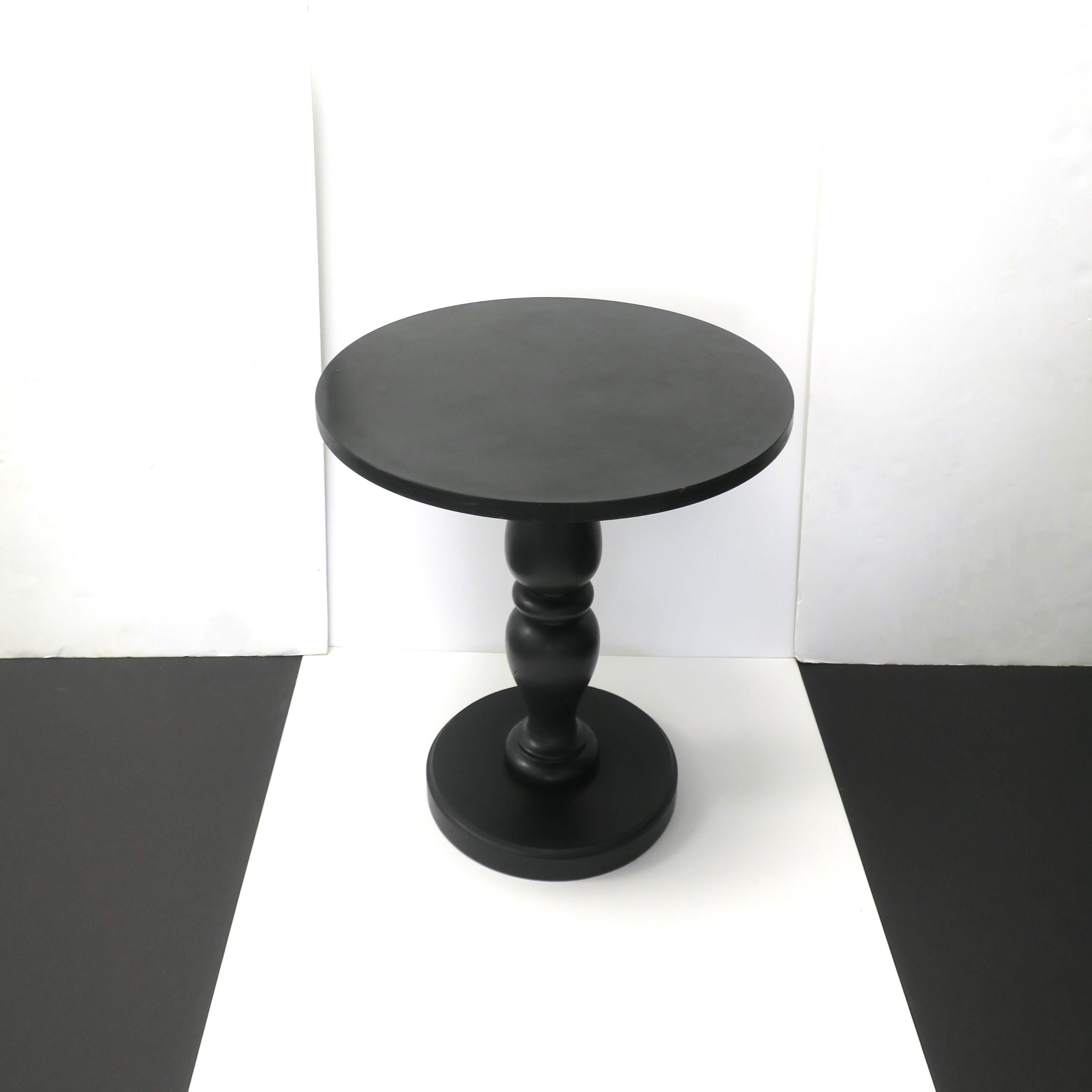 Ein runder schwarzer Beistell- oder Akzenttisch mit gedrechseltem Sockel, circa Ende des 20. Jahrhunderts, 1970er Jahre. Der Tisch hat eine hochglänzende schwarze Laminatplatte über einer Holzplatte und einen flachen oder matten gedrechselten