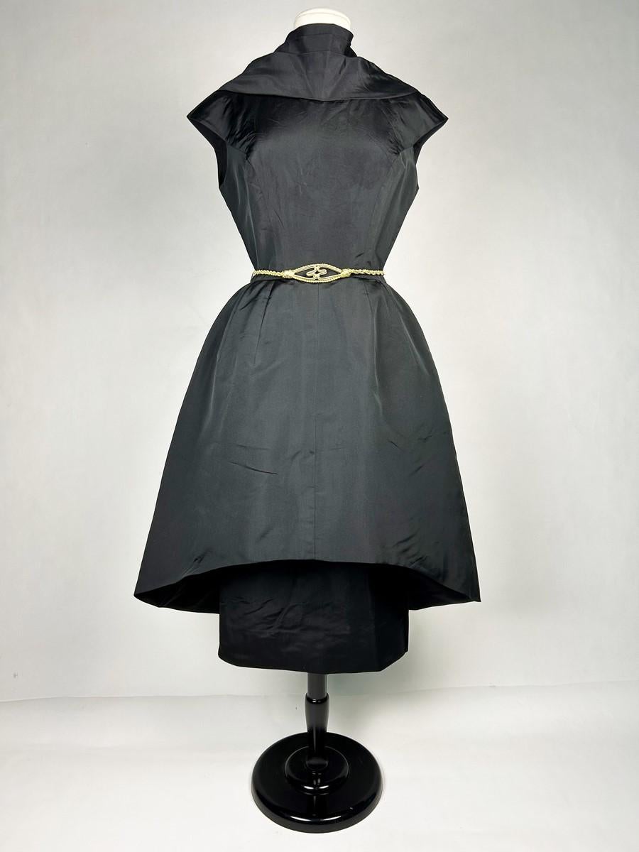 Circa 1950-1955
United States
Black silk faille cocktail dress by Pauline Trigère, a rare American couture label dating from the early 1950s. The dress is cut with a sleeveless, curved bustier and three draped pleats at the neckline, forming a