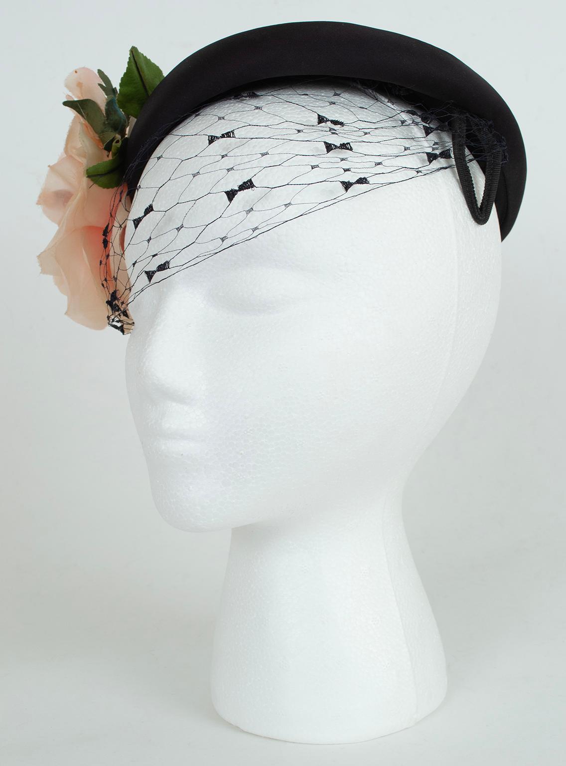 Cappello a federa basso con velo sulla fronte; tre rose di seta e velluto rosa pallido (due boccioli e un grande fiore) e steli sulla tempia destra. Fascia e fili per le orecchie in gros-grain nero. Foderato in gros grain nero.

materiale:  peau de