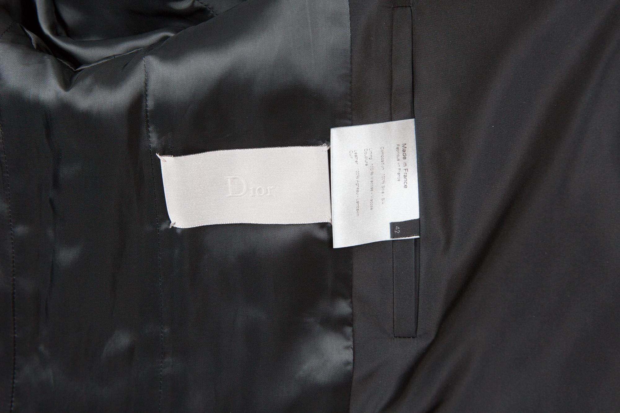 Trench-coat en soie noire de Hedi Slimane pour Christian Dior Homme avec  ceinture et épaule en cuir noir détails en cuir libre, poches latérales, double boutonnage avec boutons logo.
Il fait partie de la Collection Unisexe.
Composition :  100% soie