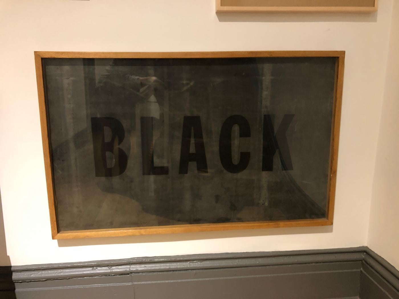 Silk screen of the word, black, on black latex. Framed in an old school style oak frame which makes it appear like a blackboard. Swiss born artist and designer, Barbara Hitz, made 20 of these in 1997.