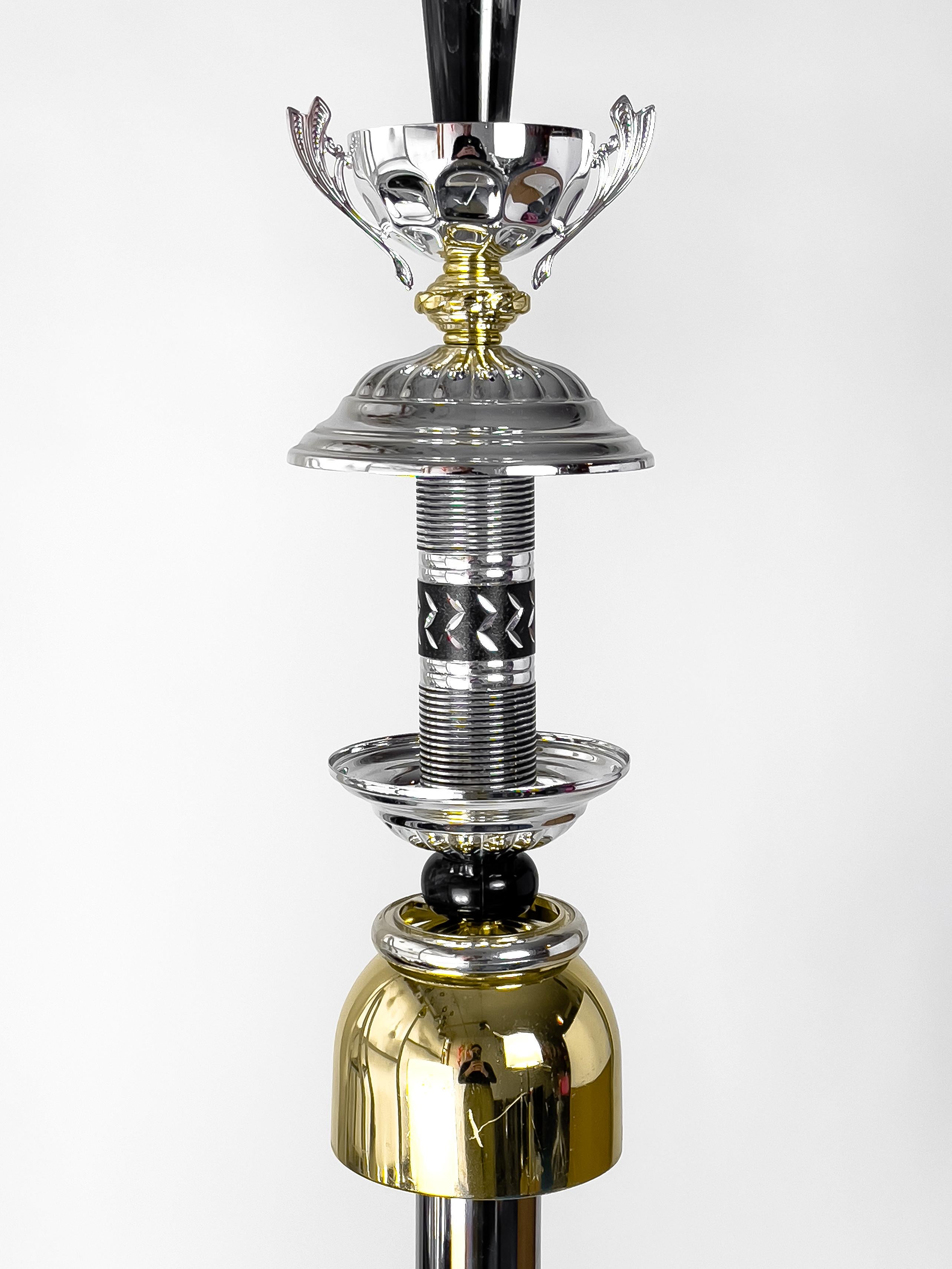 Lampada L70 nera e argento di Flétta
Dimensioni: D 10 x H 54 cm (le dimensioni sono variabili)
Cavo: 250 cm
Materiali: argento, oro

Trophy è una collezione di tavoli, luci, vasi da fiori e scaffali realizzati con vecchi trofei raccolti da