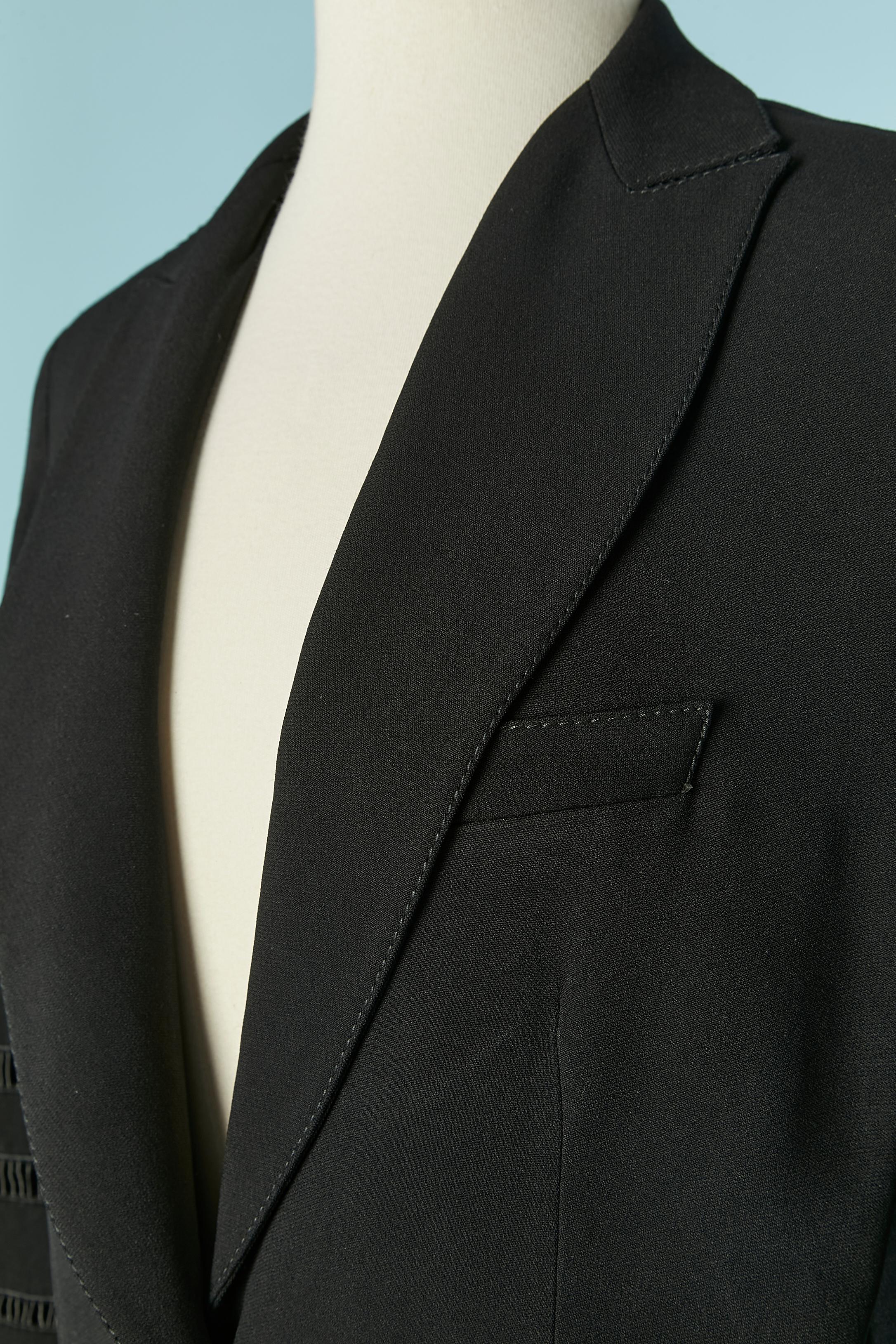 Chaqueta negra de un solo pecho con piel en la manga. Composición del tejido exterior: 50% acetato, 50% rayón. No se indica la composición del forro, pero probablemente sea acetato o rayón.
Hombrera. Botón forrado de tela y cierre de ojal en el