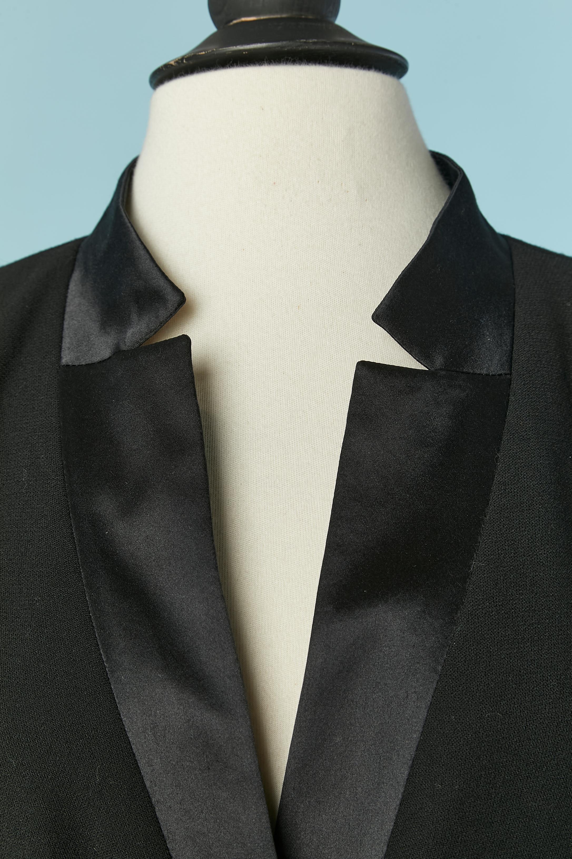 Giacca monopetto nera con collo in seta. Tessuto principale: 100% lana. Fodera con marchio: 95% seta, 5% elastan. Spallaccio. Catena all'interno della giacca sul bordo inferiore. Un bottone e un'asola di marca sulla parte centrale del davanti e 4