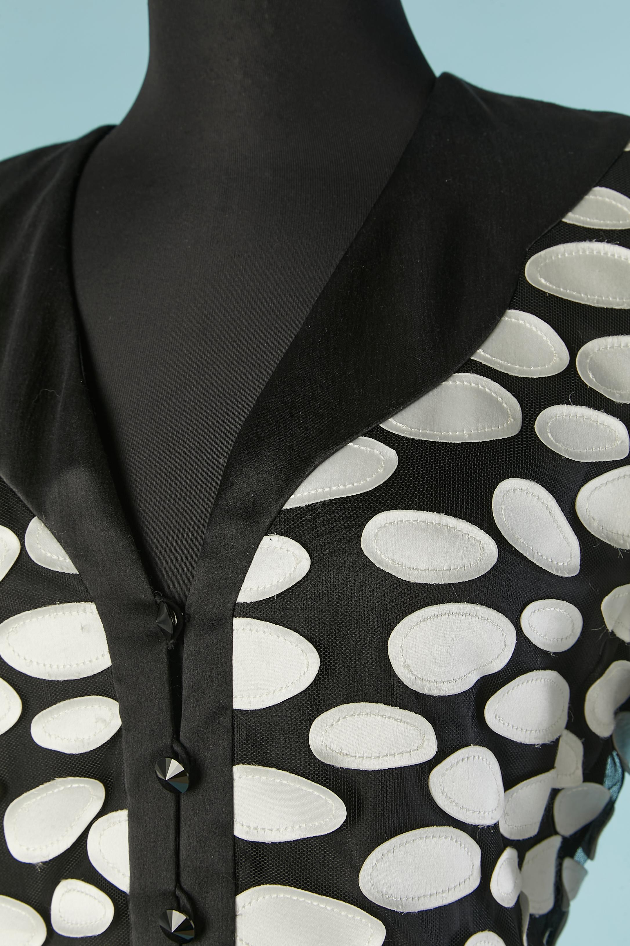Black skirt-suit with white silk appliqué on the jacket. Main fabric composition: 80% polyester, 11% silk, 1% cotton. 
Tulle ruffles on the sleeve edge. Shoulder pad. Button and buttonhole closure on the middle front. 
SIZE M 
