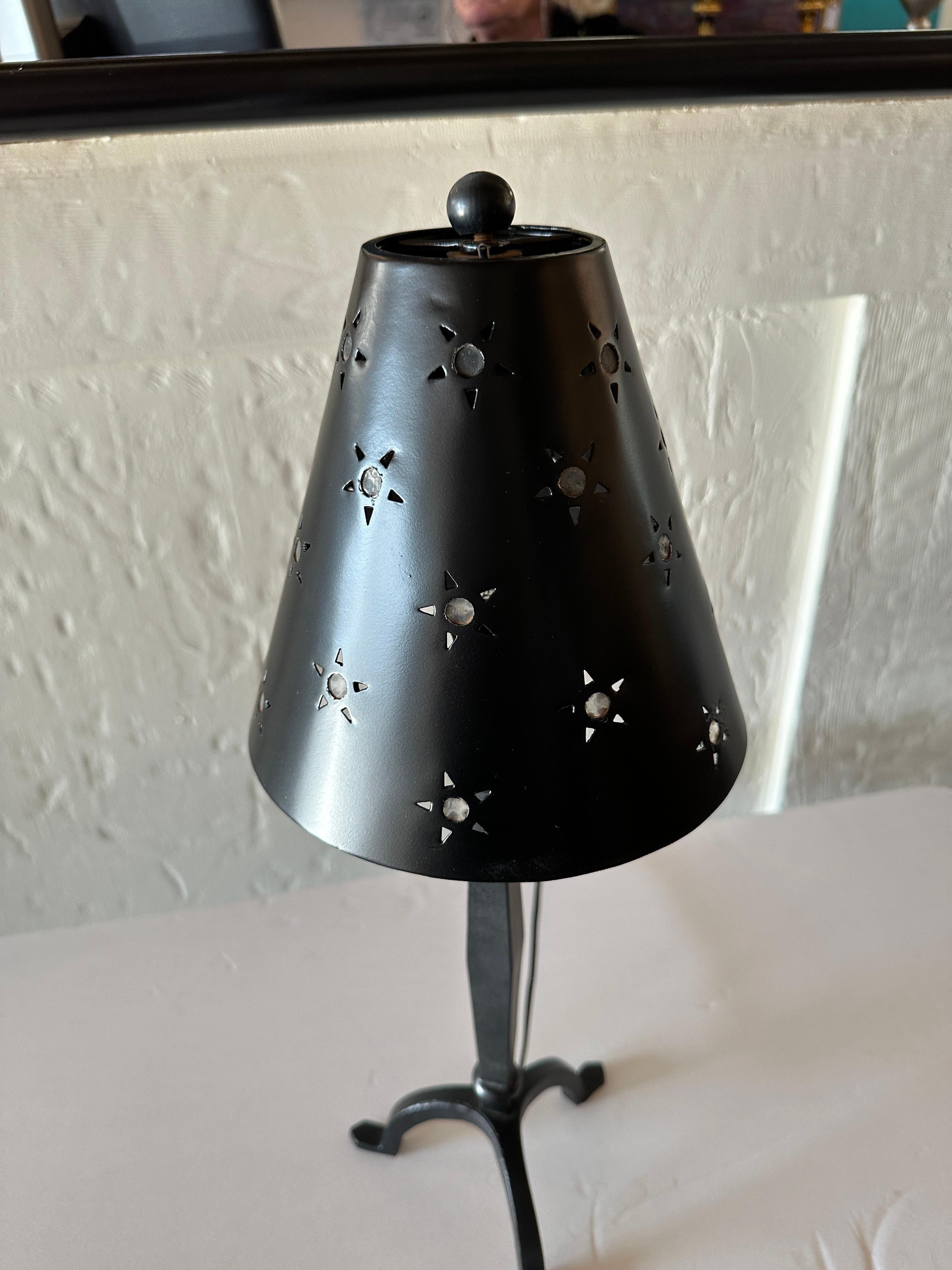 This mini table lamp has a sleek black base with three gracefully curved legs in the same flat black finish as the lamp's body and shade.
The shade features a unique pattern, with hollow stars scattered across its surface. These stars, each