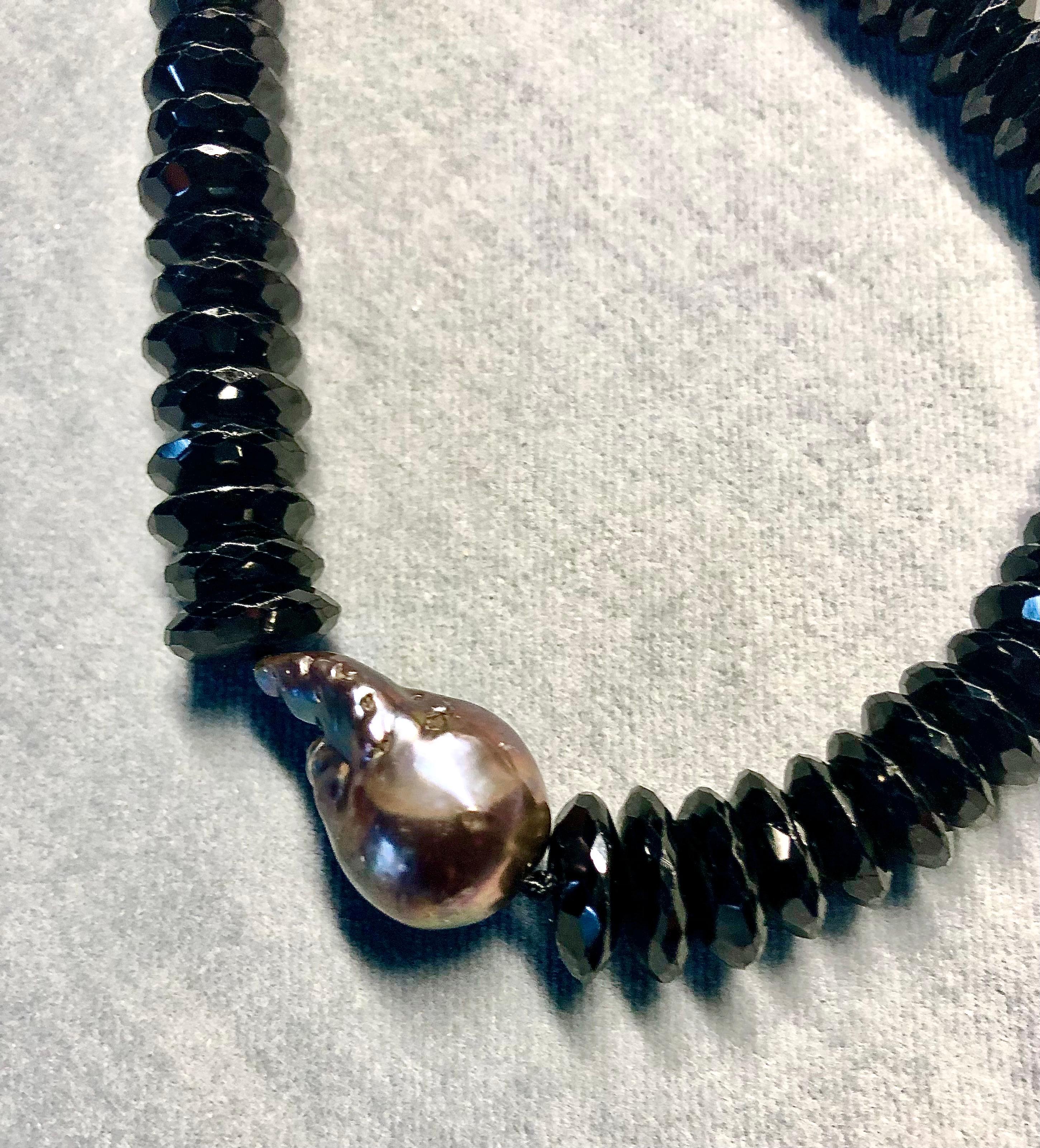 Single strand 18” necklace of very fine sharply defined German cut glistening black spinels 10.5-8.25 mm.
Center focal point is a large freshwater cultured, highly lustrous grey pearl with mauve and green under tones. Finished with a gunmetal color
