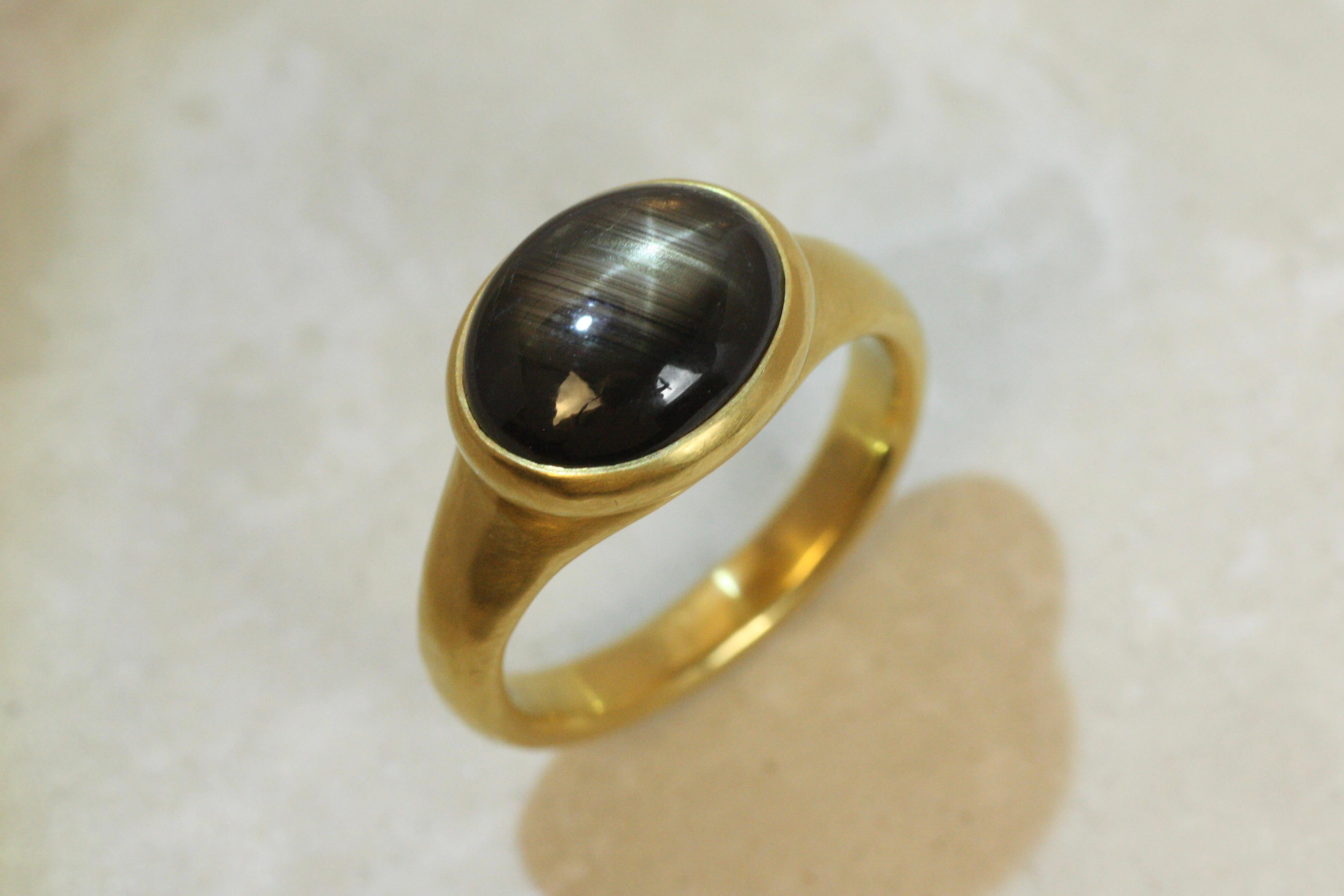 Mystique et envoûtant, ce saphir noir étoilé de 6,92ct rayonne d'un charme céleste avec son astérisme naturel formant un reflet étoilé sous la lumière. Sertie dans un chaton lisse en or jaune 22 carats, cette bague solitaire fabriquée à la main est