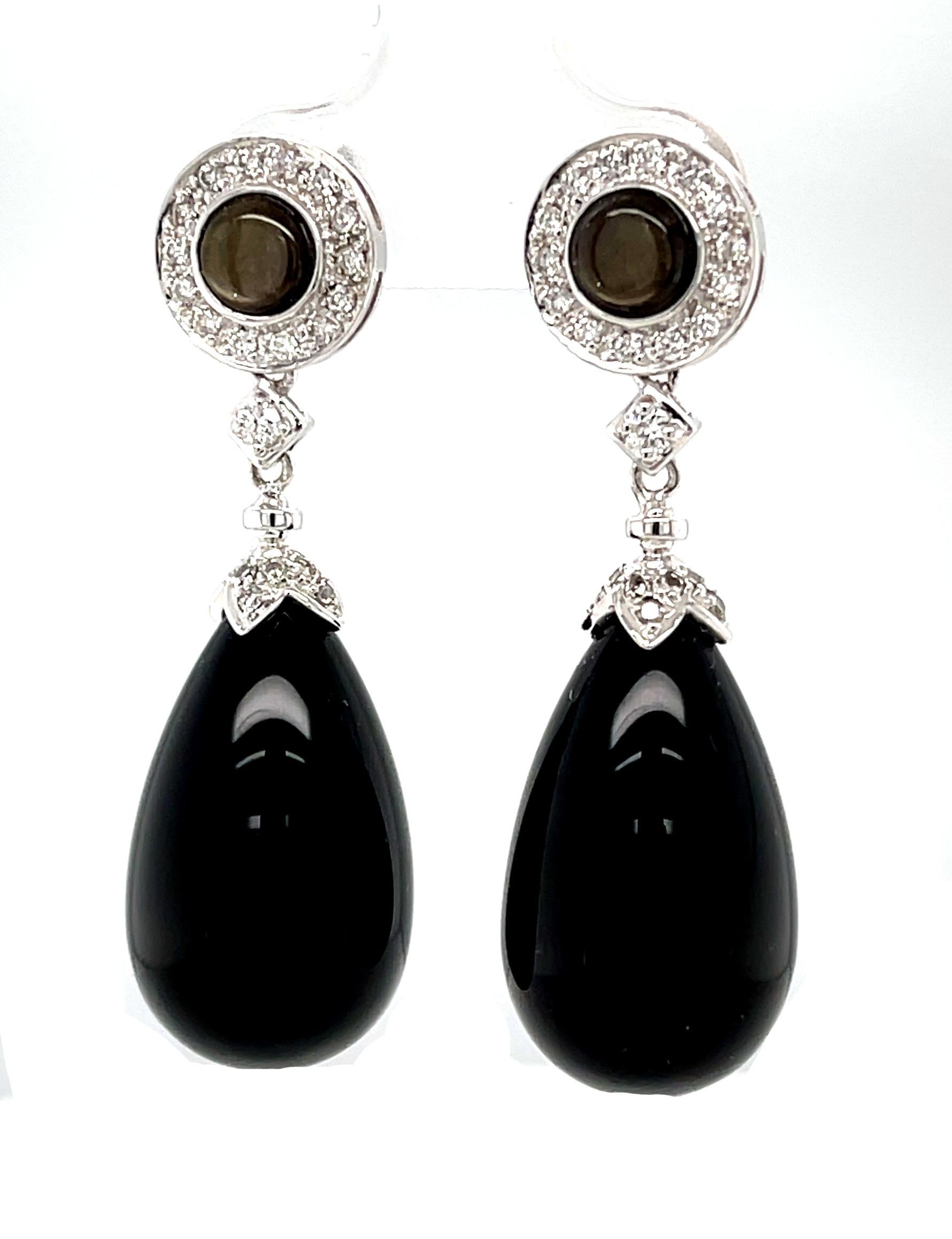 Black onyx pendalogues are topped with tiny diamonds and suspended from black star sapphires in these elegant white gold dangle earrings. The black star sapphires are encircled with diamonds making a striking combination of colors, shapes and
