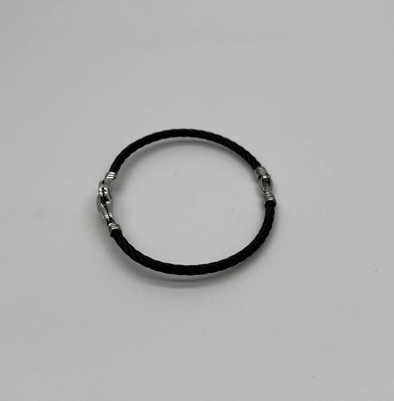 This elegant bracelet features a twisted cable design in black and 18K white gold parts. The centerpiece is a polished metal clasp adorned with intricate detailing and sparkling accents. The bracelet's sleek and modern aesthetic is complemented by