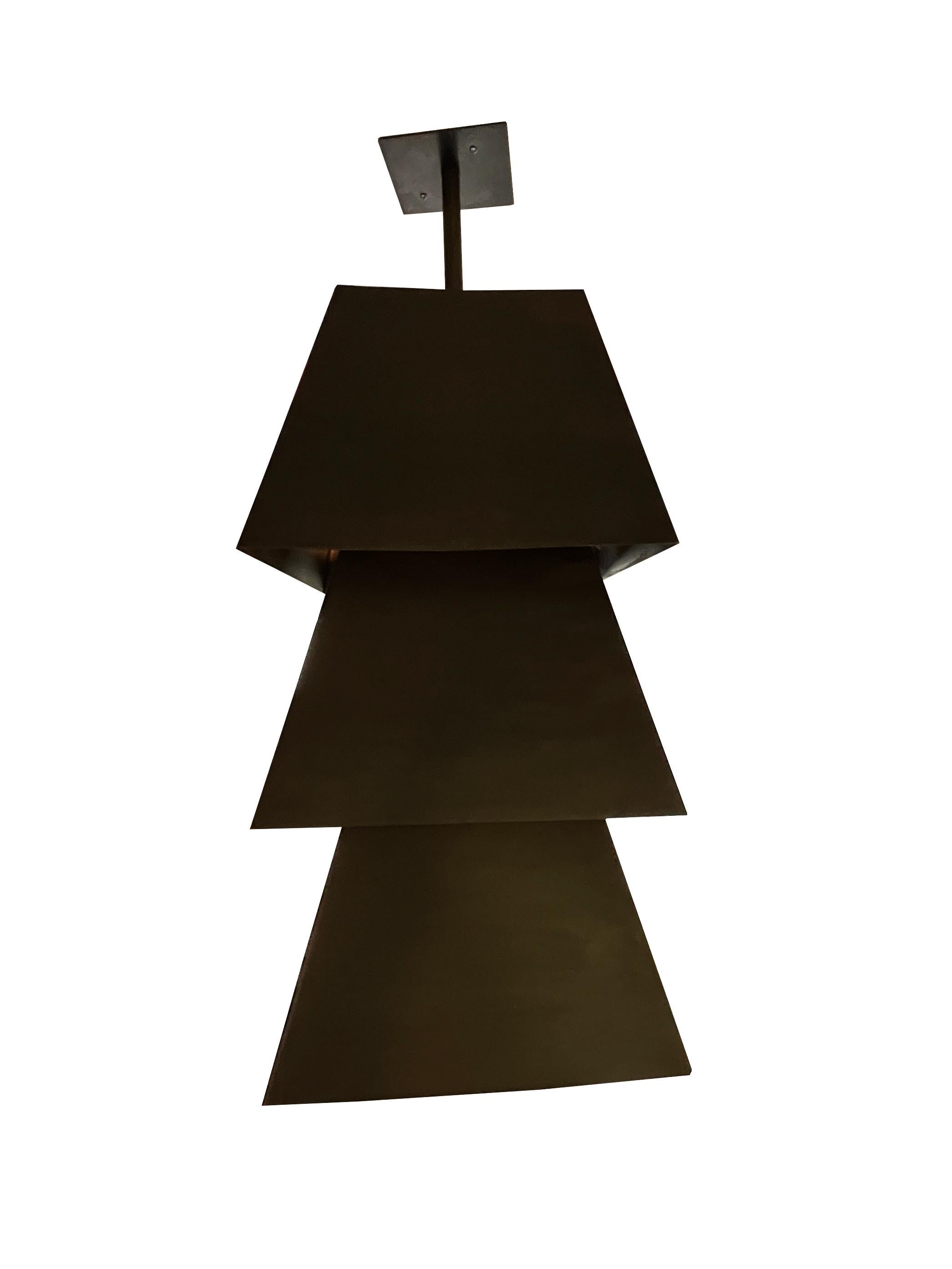Volumetrisch gestapelte trapezförmige Deckenleuchte aus schwarzem Stahl von Juan Montoya Design. Diese Deckenleuchte lässt das Licht durch 3 Öffnungen scheinen, was sie nicht nur funktional, sondern auch zu einer skulpturalen Leuchte macht. Diese