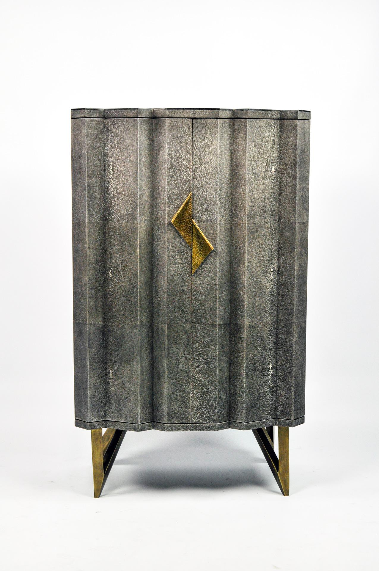This cabinet has two doors and it is made of black stone marquetry on top and sides. The doors are made of shagreen in a dark grey color, with casted brass handles.
The feet are in metal with a bronze patina.

The interior with 2 shelves is in