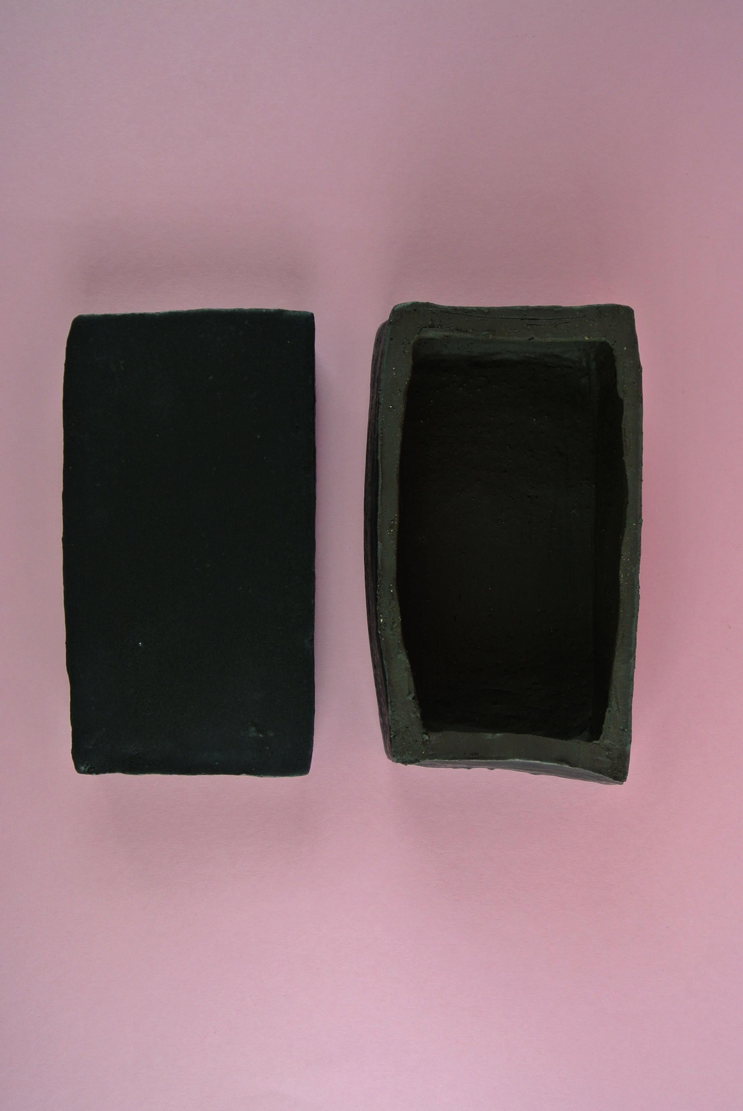 Asymmetric black stoneware box with lid and black matte glaze. Smooth texture with sporadic traces of fire sand visible on the surface and through the glaze. The box is only glazed on the outside. 
Please inquire for more information about other