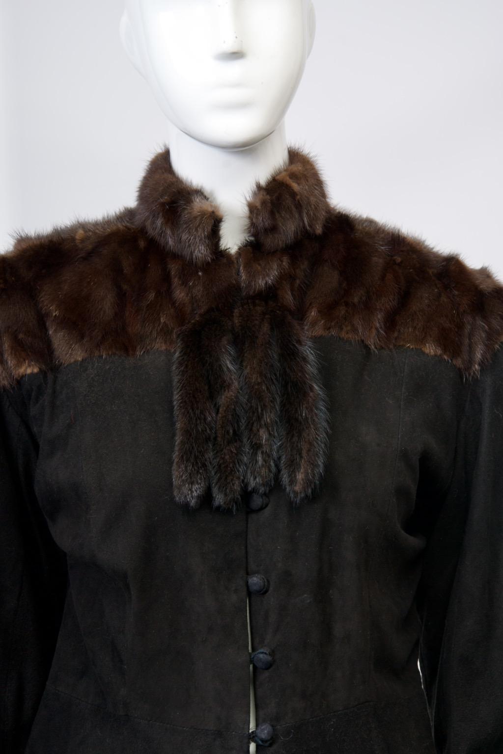 A novel vintage piece from the 1980s, this jacket is crafted of supple black suede and features a yoke, mandarin collar, and two pairs of tails at the neck of dark brown mink. The set-in sleeves taper to the wrist, where they are trimmed with