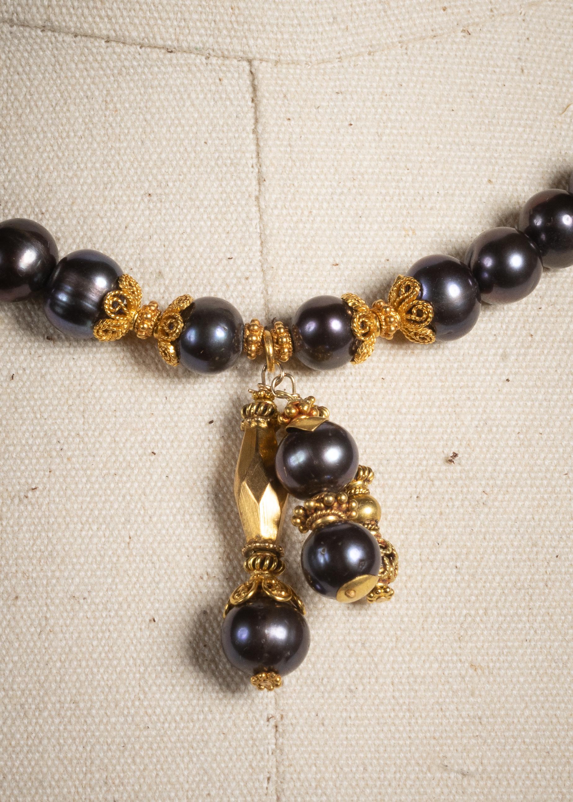 Una sexy collana di perle di Tahiti nere da 8-9 mm con terminali in oro 22K lavorati a filo tra le perle. Il centro presenta tre gocce sfalsate di perle e perline d'oro 22 carati ed elementi lunghi 1,5
