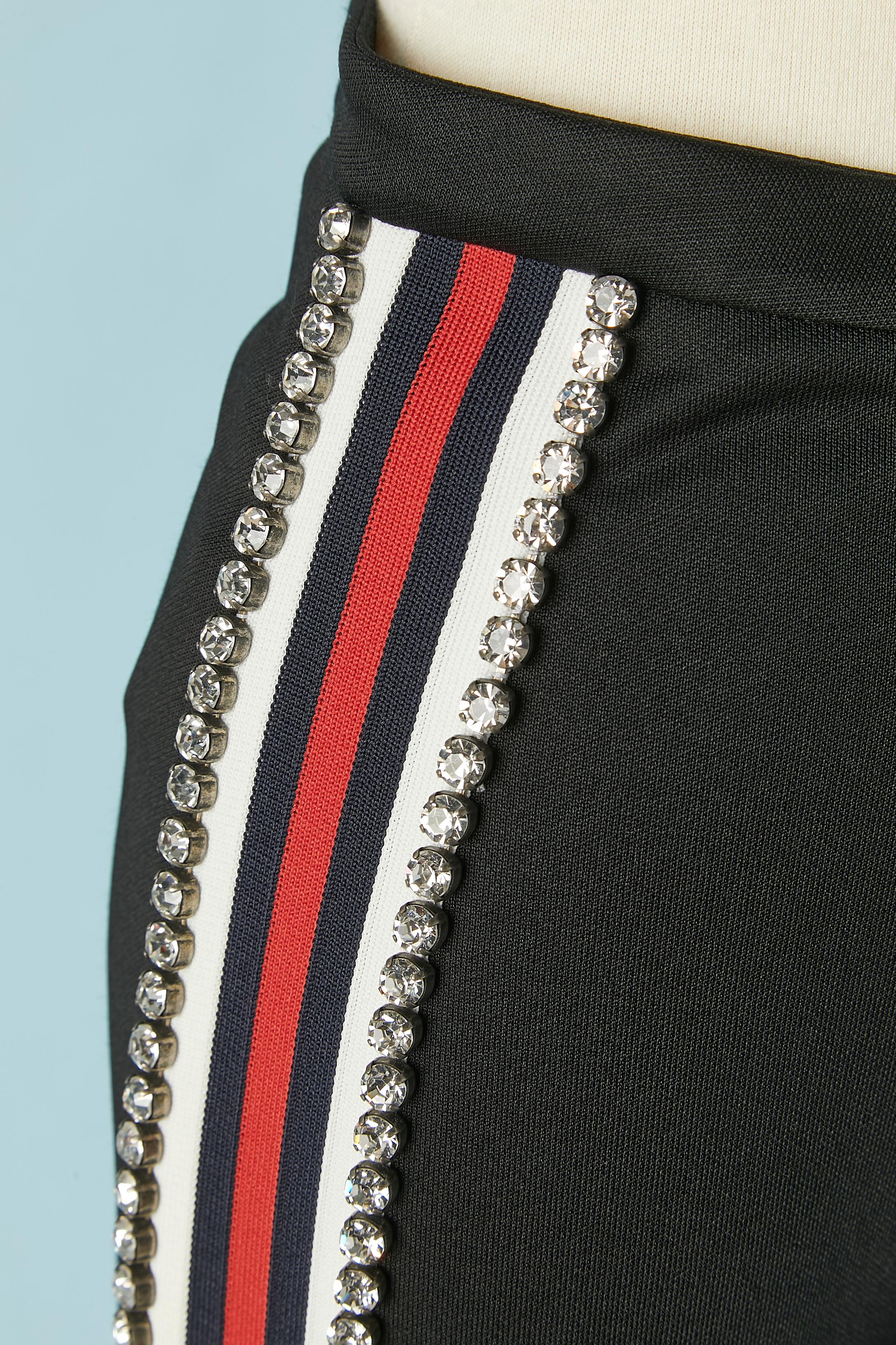 Black tapered trousers with striped and rhinestone trimming. Detachable Band passing under the foot. Zip , button and buttonhole closure on the top middle front. Zip at the end of the legs inside. 
Main fabric composition: 55% polyester, 45% cotton.