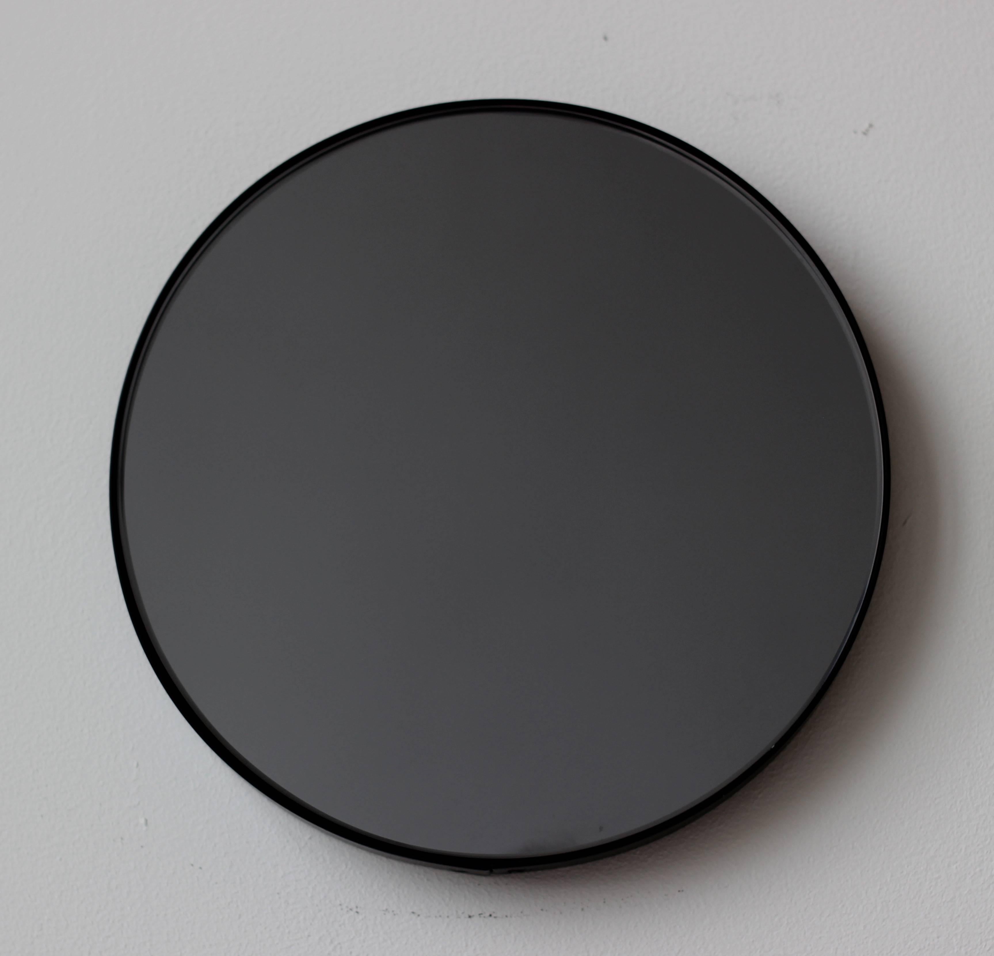 Zeitgenössischer Orbis™ runder, schwarz getönter Spiegel mit einem minimalistischen, schwarz pulverbeschichteten Aluminiumrahmen. Entworfen und handgefertigt in London, UK.

Die mittelgroßen, großen und extragroßen Spiegel (60, 80 und 100 cm) sind