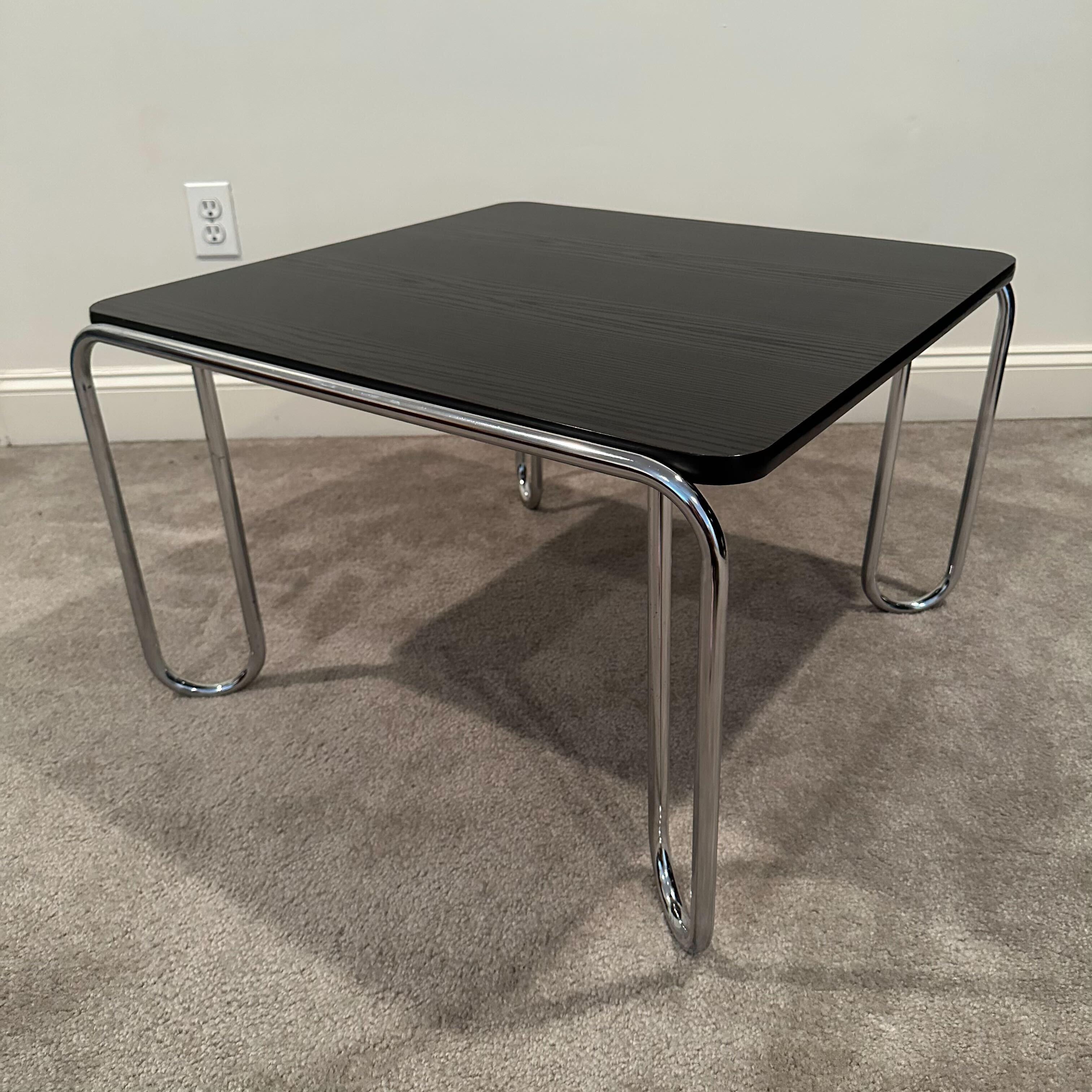 A square black faux wood tabletop supported by looping tubular chrome bar legs, this coffee or cocktail table is in the Modernist or Bauhaus style of Marcel Breuer. The black laminate tabletop is embossed with a textured faux wood grain. Polished