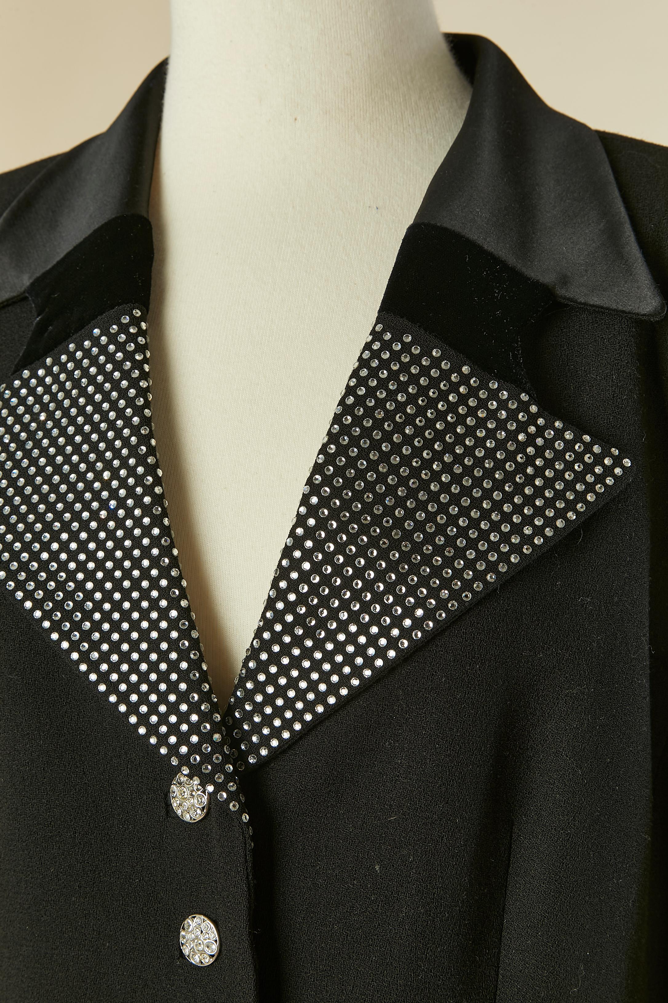 Chaqueta de esmoquin de lana negra con cuello de pedrería, satén y terciopelo. Forro de cupro. 
Botón de strass y ojal en el centro delantero. Bolsillo a ambos lados con solapa de brillantes. Dividida por la mitad de la espalda con 2 botones de