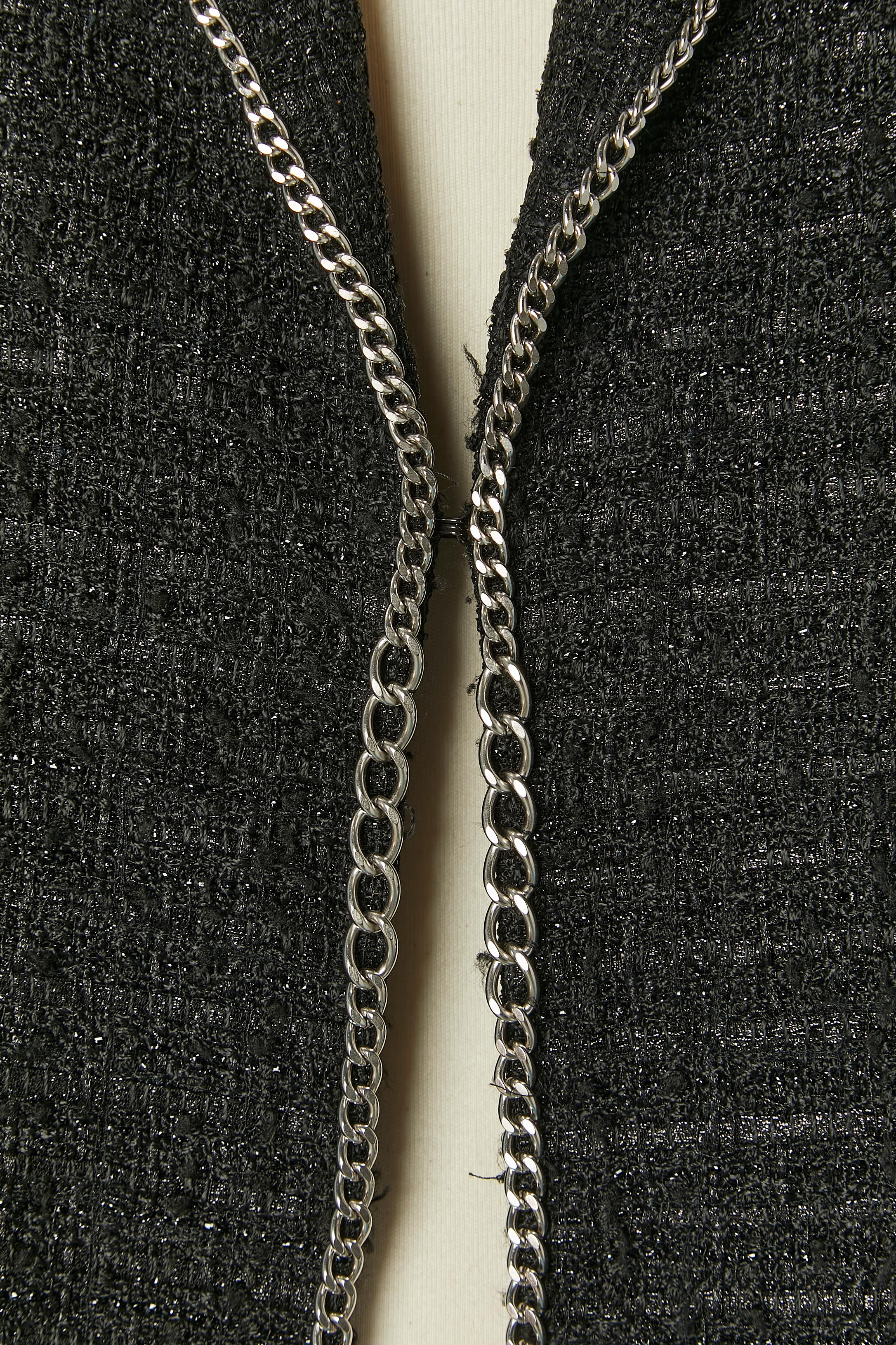 Giacca in tweed nero e nylon con bordo a catena. Composizione del tessuto: 55% rayon, 27% poliestere, 12% nylon, 6% cotone. 
Fodera in seta. Chiusura con gancio e occhiello al centro della parte anteriore. Padiglione della spalla. 2 spaccate sulla