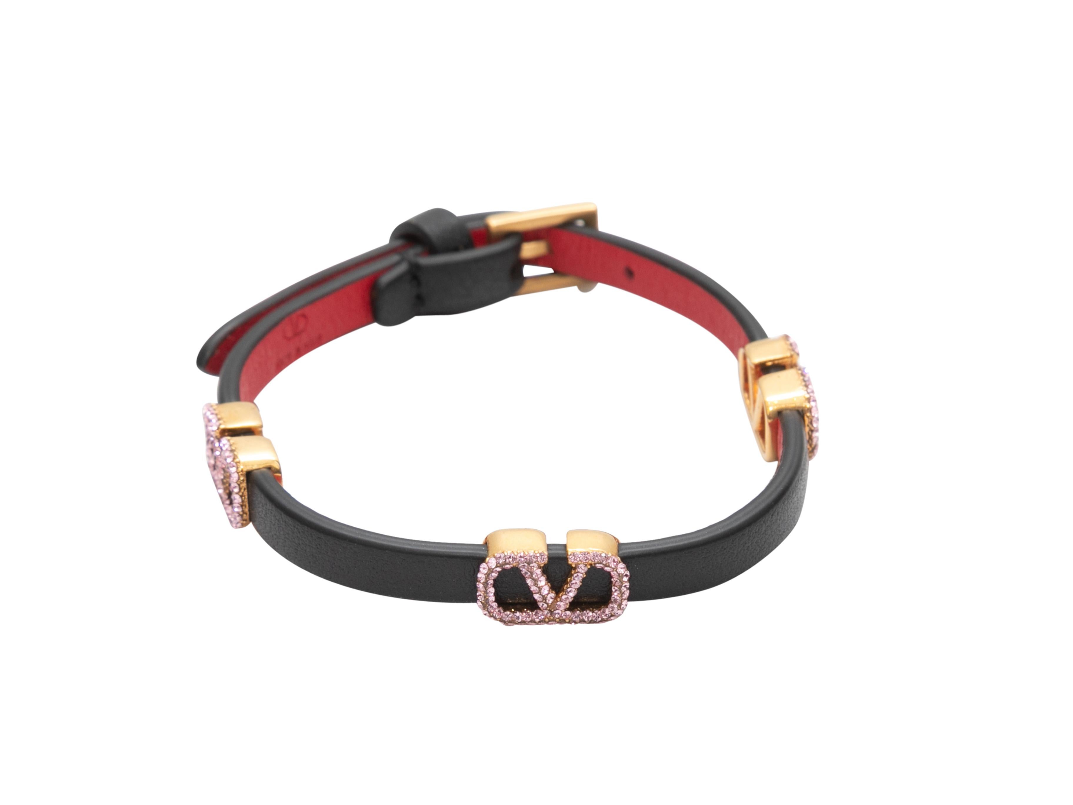 Black leather bracelet by Valentino. Gold-tone logo hardware featuring pink crystal embellishments. Buckle closure. 0.25