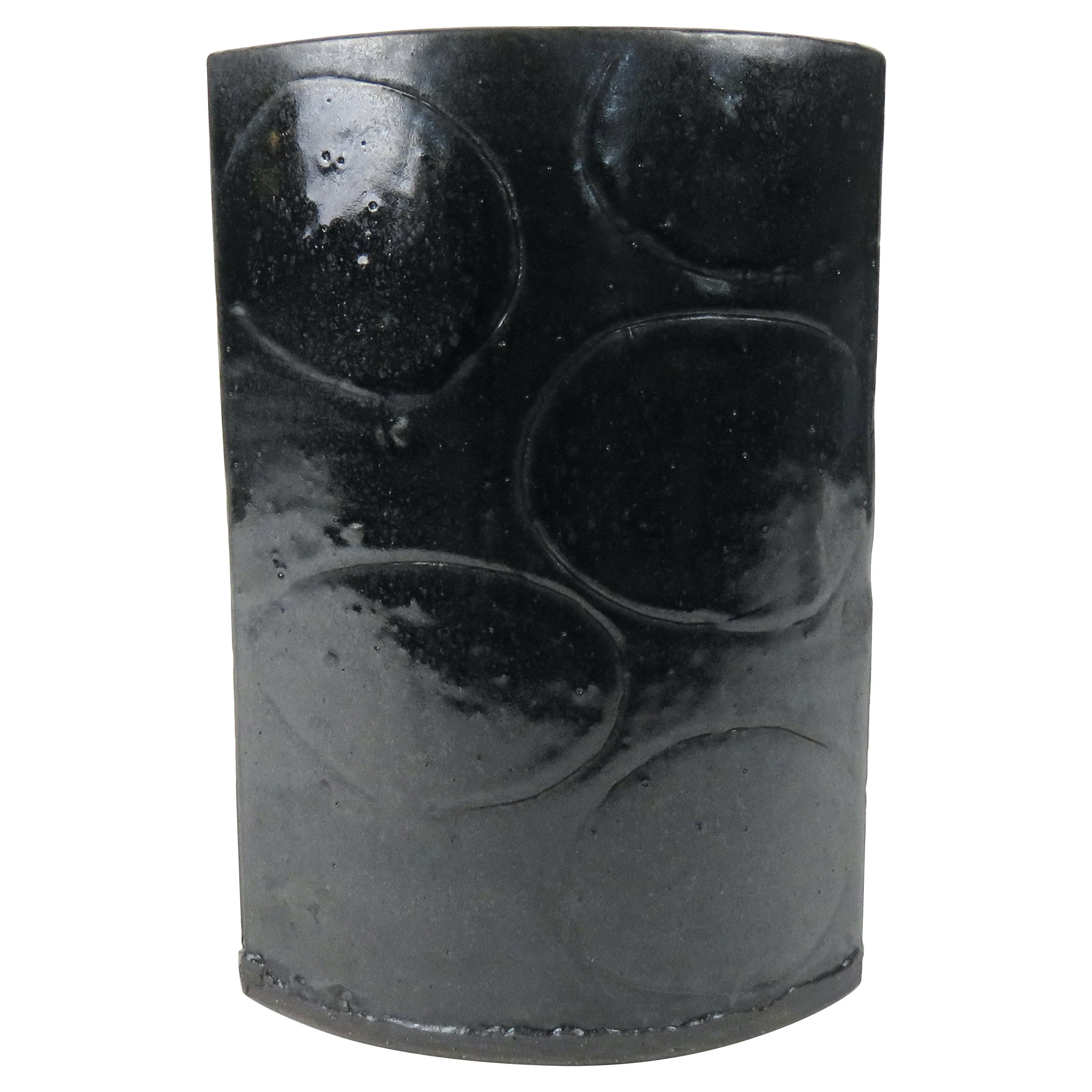 This Vase has a Luscious Black Glaze that shows speckling and depth. An original design by Artist Helena Starcevic, it consists of 2 arcing walls with hand carved designs. The dark clay is rolled out by hand, cut to size, then stood on end and