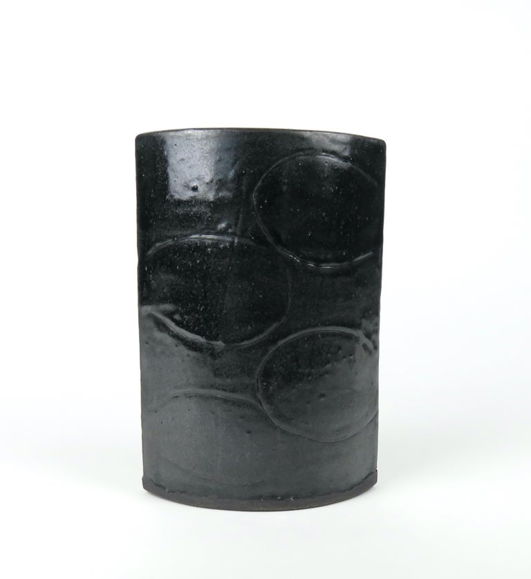 This Vase has a Luscious Black Glaze that shows speckling and depth. An original design by Artist Helena Starcevic, it consists of 2 arcing walls with hand carved designs. The dark clay is rolled out by hand, cut to size, then stood on end and