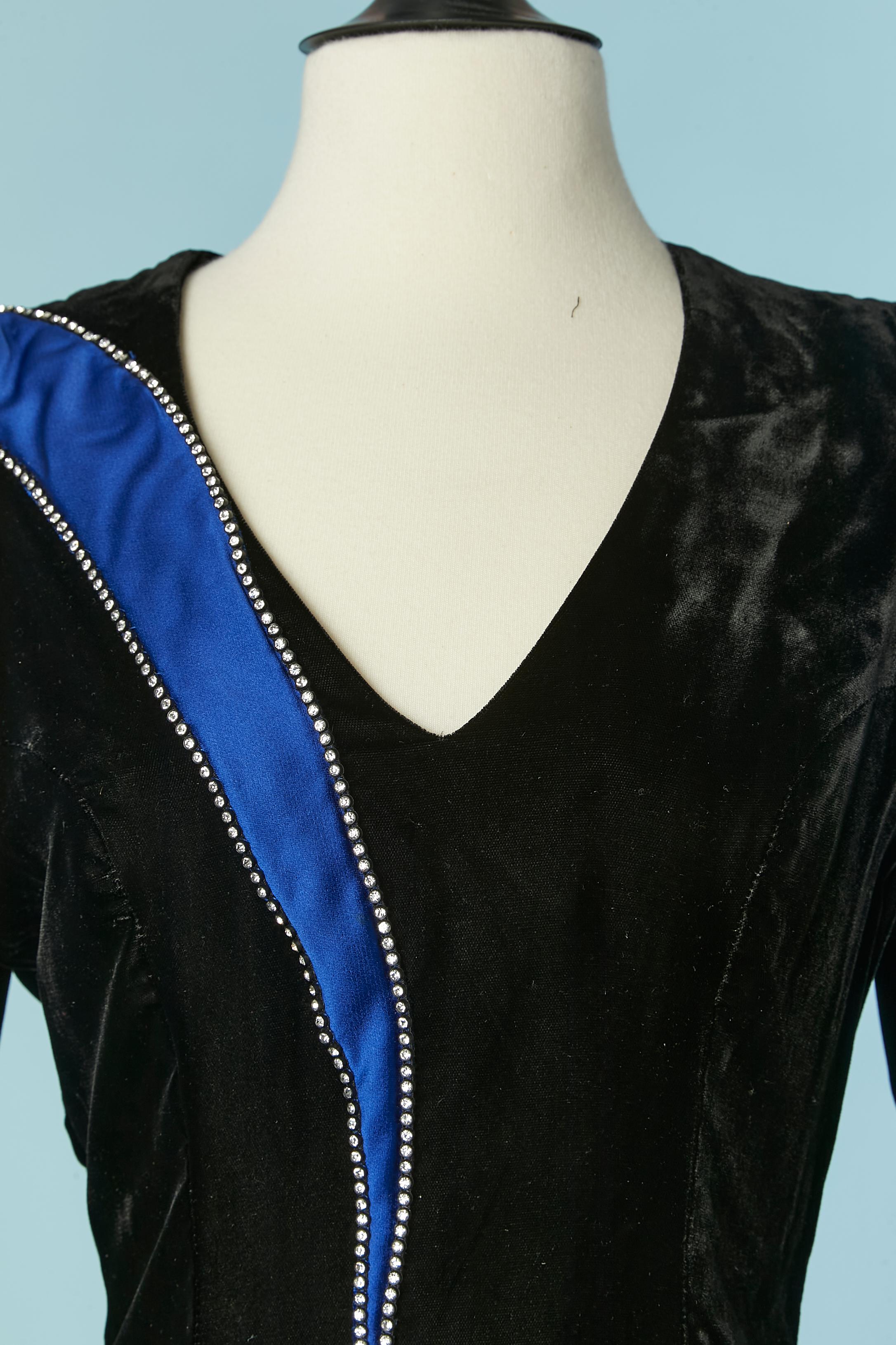 Schwarzes Cocktailkleid aus Rayonsamt mit Satineinsatz und Strassapplikation. Rayon-Futter. Reißverschluss in der hinteren Mitte und an den Ärmeln. Verstärkte Schultern und steifer Stoff in den Ärmeln, um das Volumen zu erhalten. Schlitz am unteren