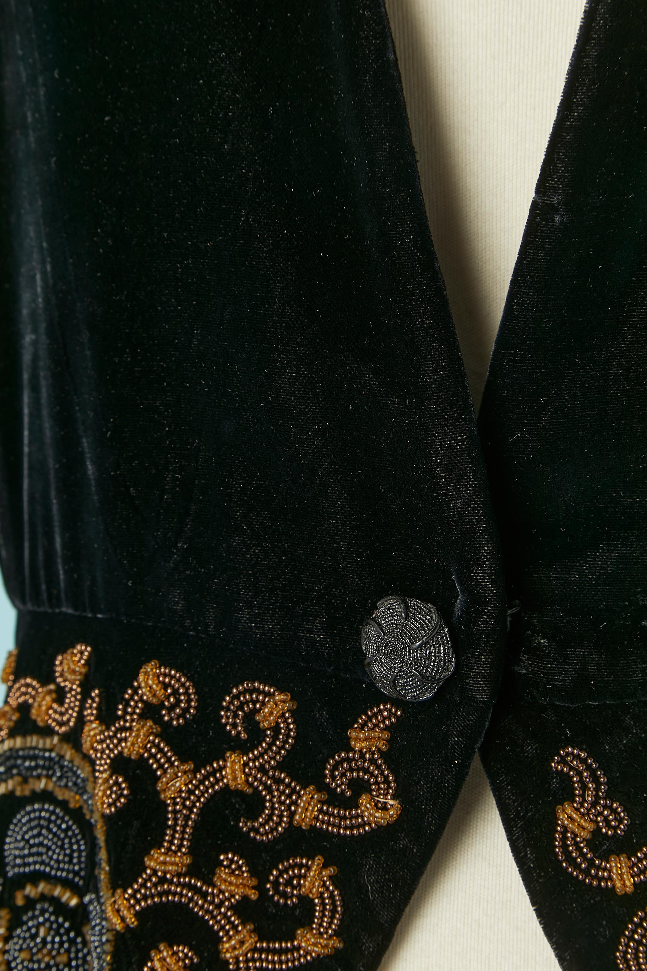 Chaqueta de terciopelo negro con trabajo de pedrería. No hay etiqueta de composición del tejido, pero el terciopelo podría ser de rayón o terciopelo de seda y el forro probablemente de acetato o rayón. 
Un cierre a presión en la parte delantera