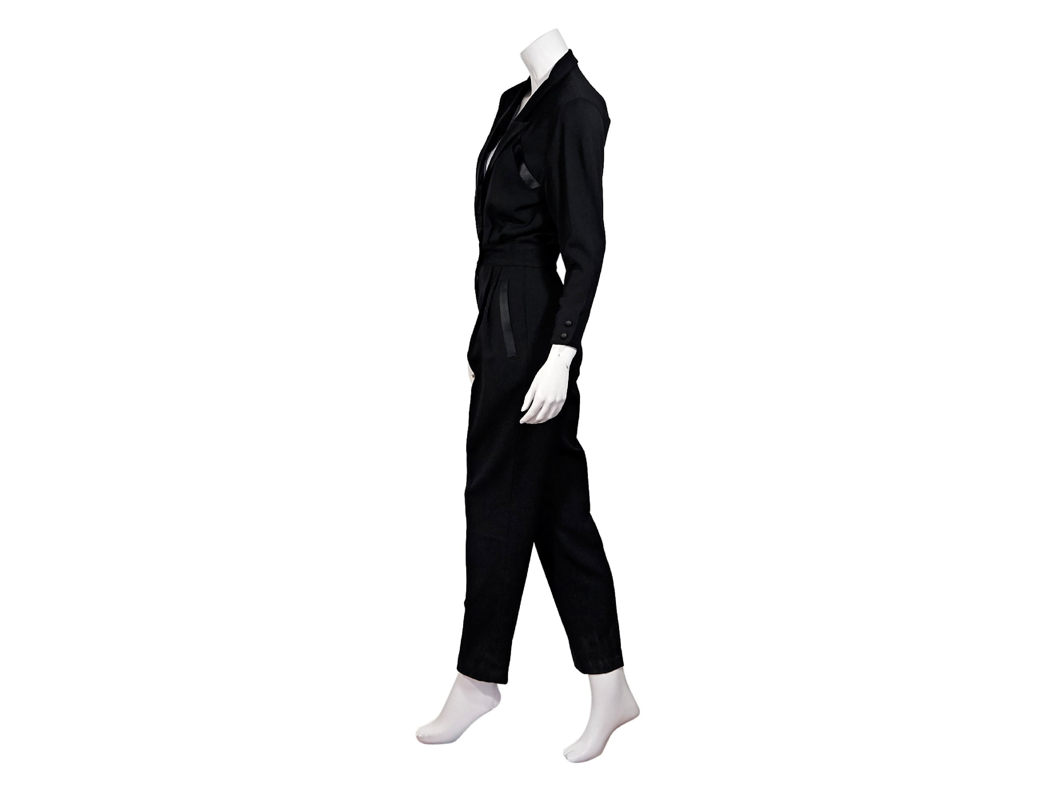 Product details:  Vintage black wool tuxedo jumpsuit by Escada.  Circa the 1980s.  Satin peaked lapel.  Three-quarter length sleeves.  Double-breasted button-front.  Chest besom pocket.  Pleats taper off banded waist.  Concealed zip fly.  Waist