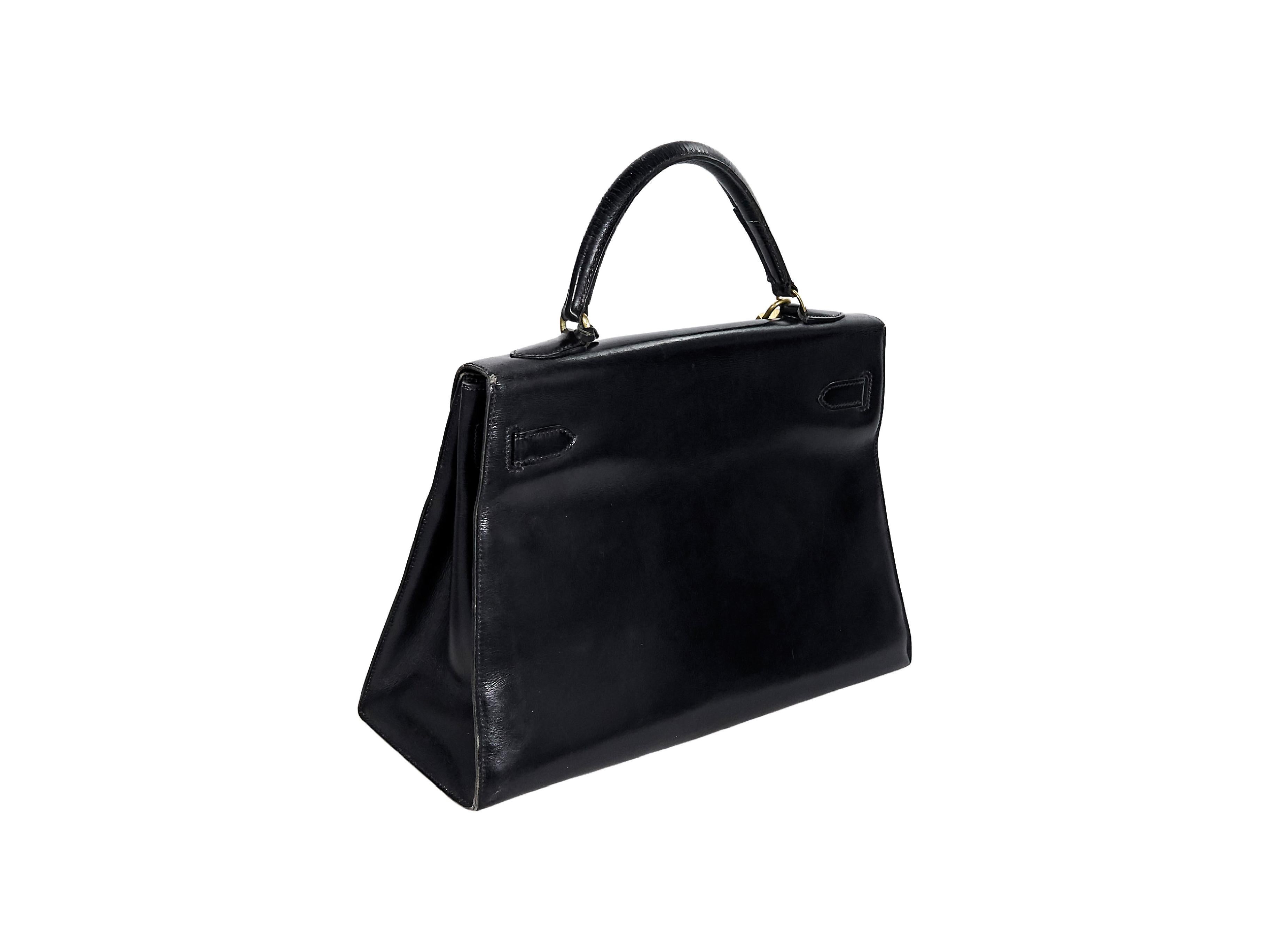 Product details:  Vintage black leather Kelly handbag by Hermes.  Top carry handle.  Front flap with lock-and-key strap closure.  Leather interior with slide pockets.  Protective metal feet.  Goldtone hardware.  12